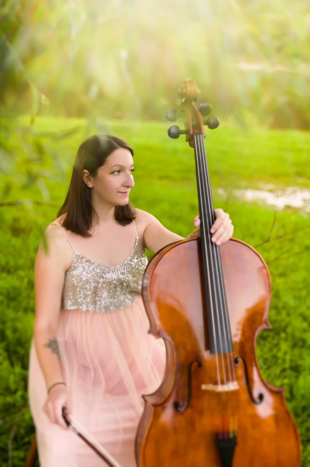 Woman wearing a sequin and tulle dress playing a cello in a garden setting.