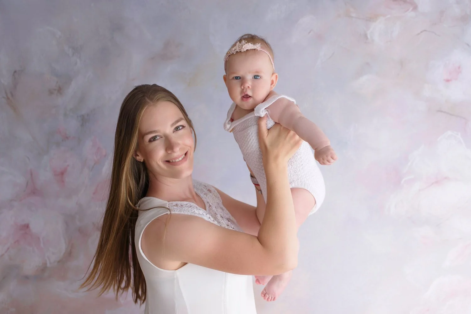 Smiling woman holding a baby in front of a pastel-colored background.