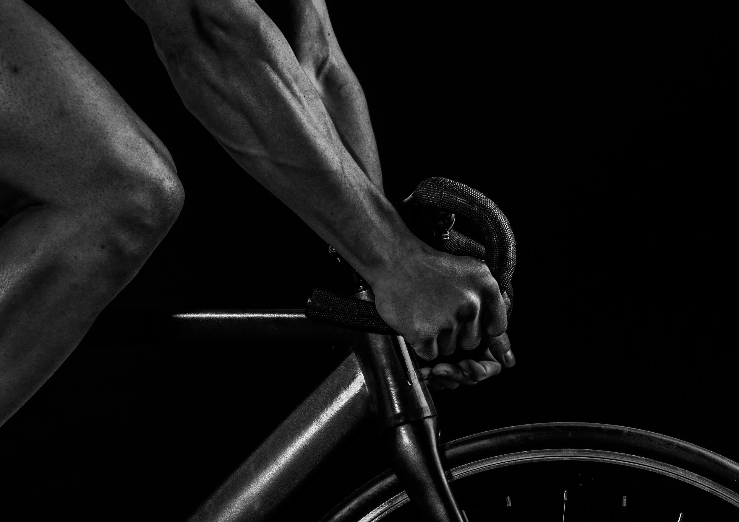 Black and white photo of a cyclist's hands gripping handlebars on a bicycle with emphasis on the arm muscles.