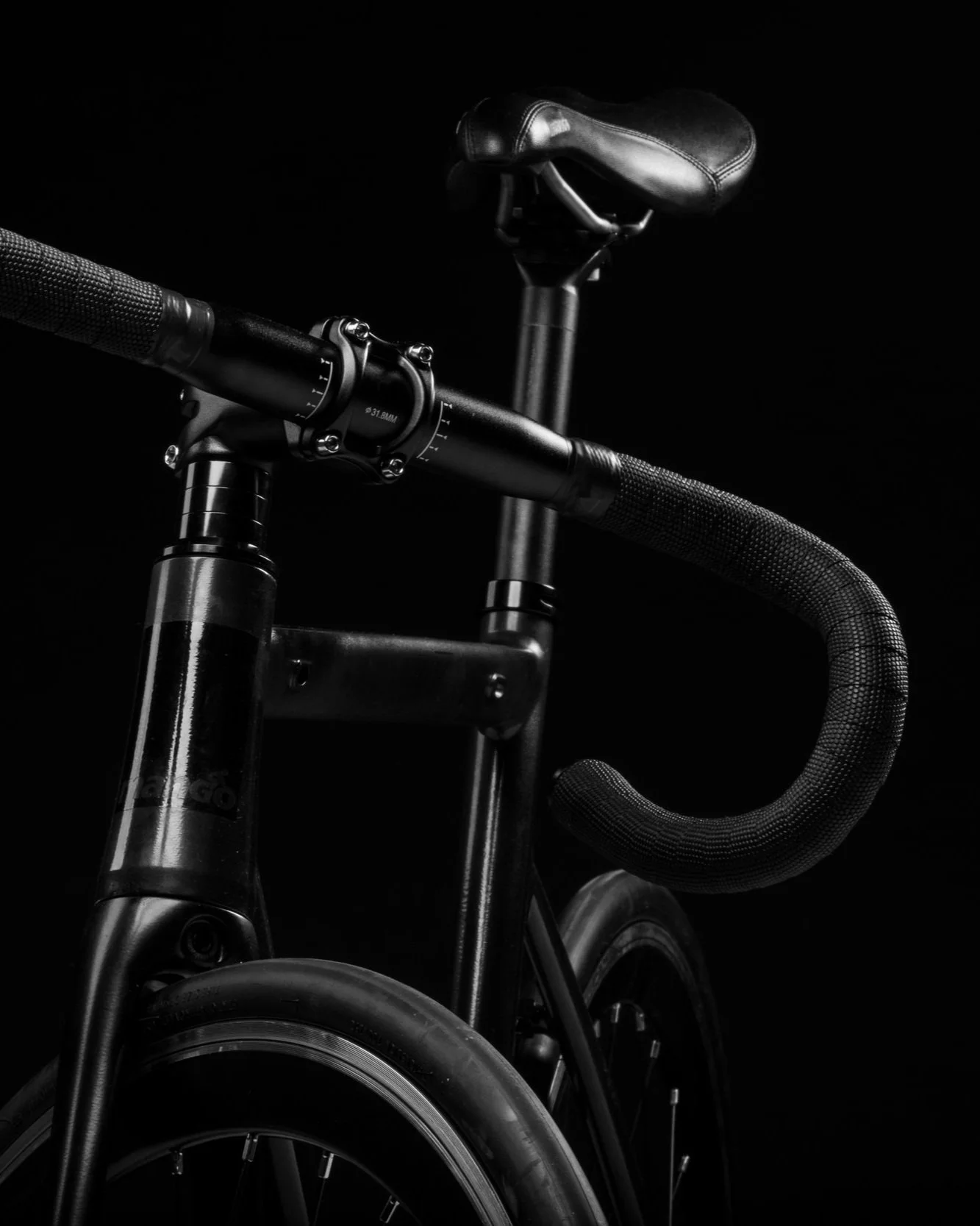 Close-up of a black bicycle handlebar, seat, and front wheel against a dark background.