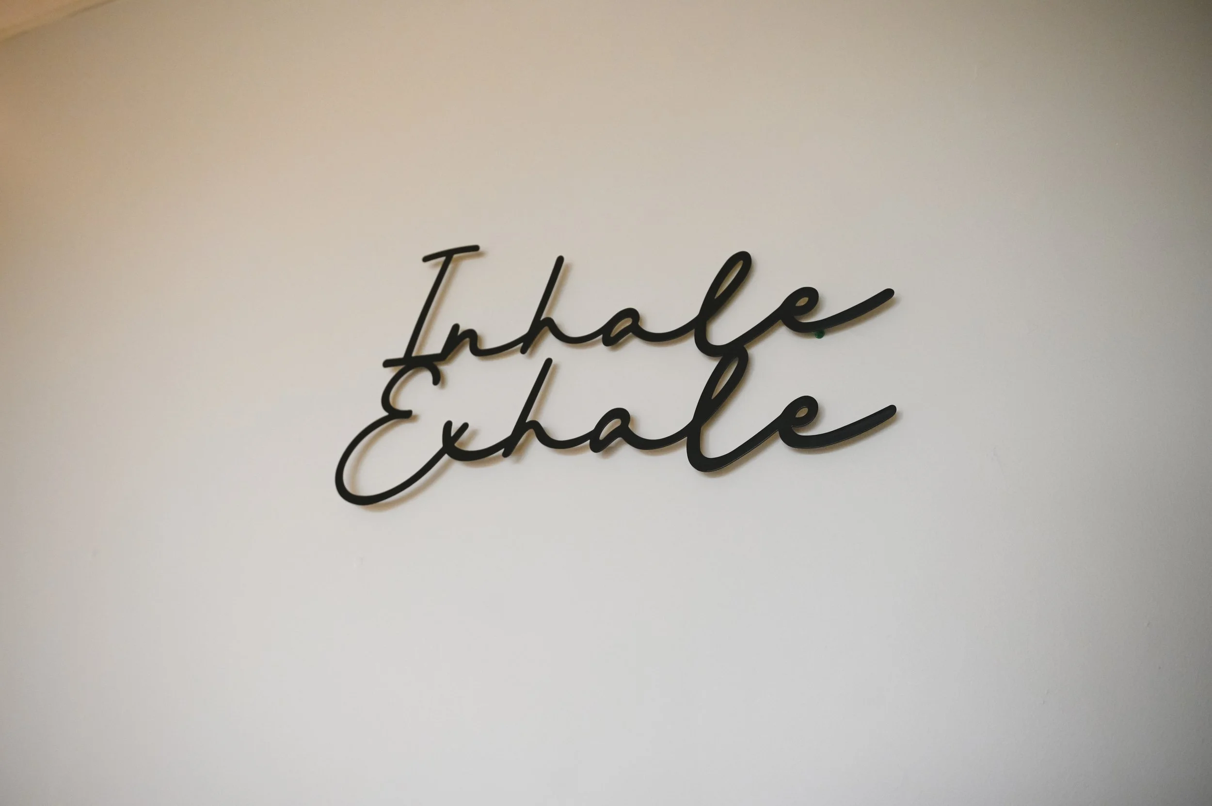 Metal wall art with the words 'Inhale Exhale' in cursive.