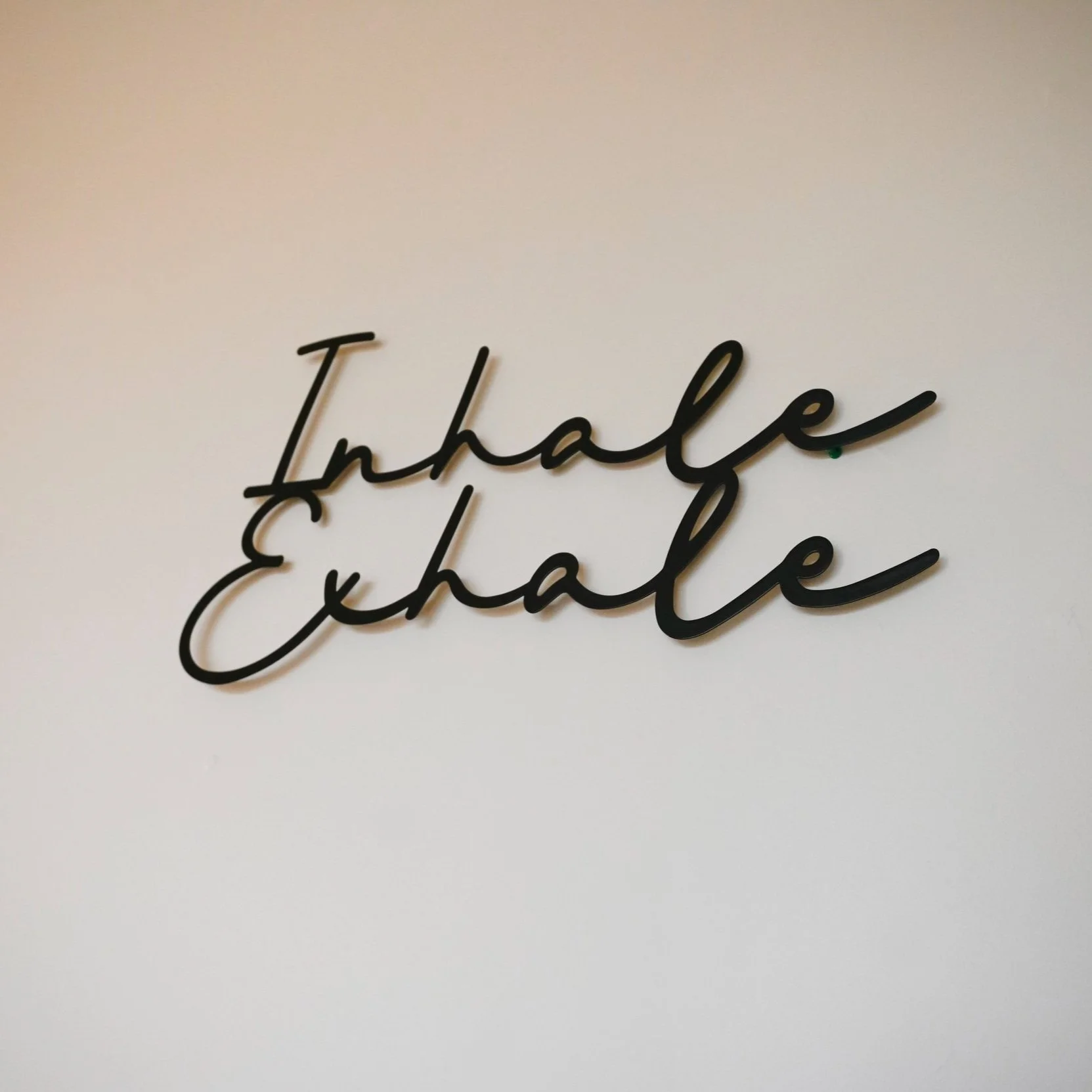 Black cursive text on a beige wall saying 'Inhale Exhale'