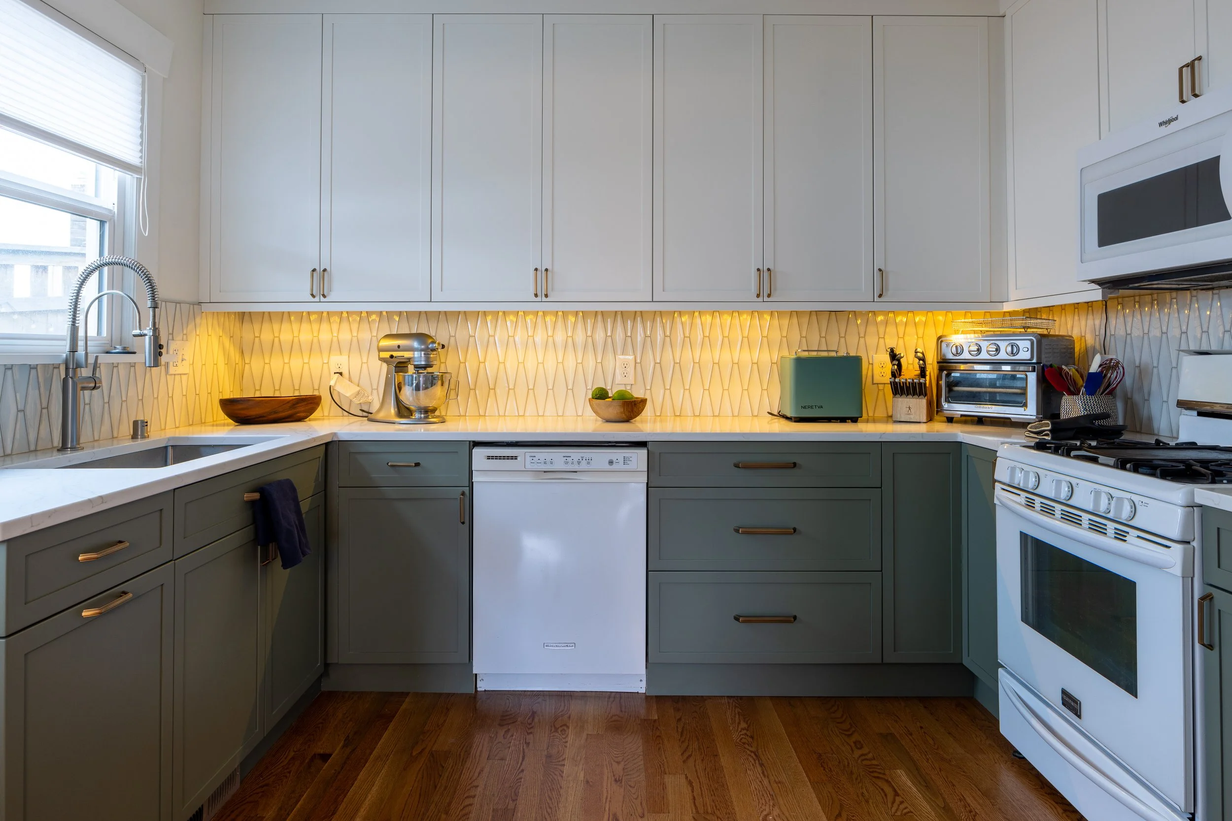 Green lower cabinets and white upper cabinets, quartz countertops, tile backsplash
