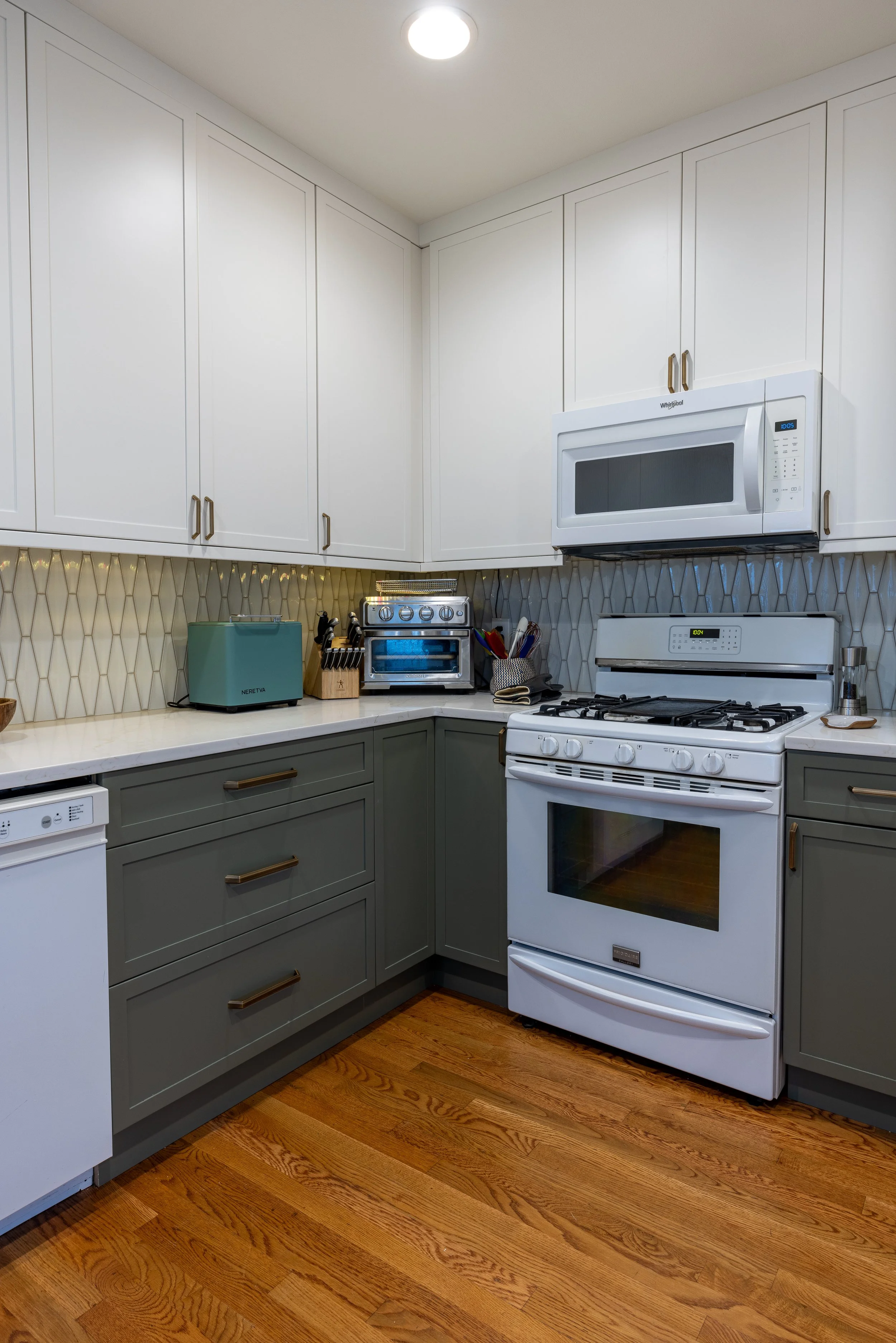 Green lower cabinets and white upper cabinets, quartz countertops, tile backsplash