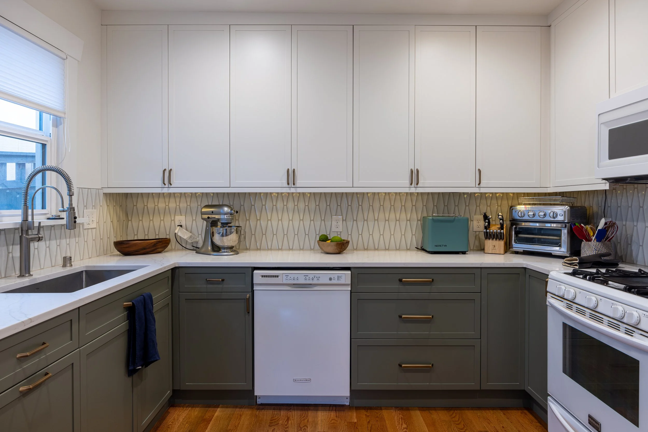 Green lower cabinets and white upper cabinets, quartz countertops, tile backsplash