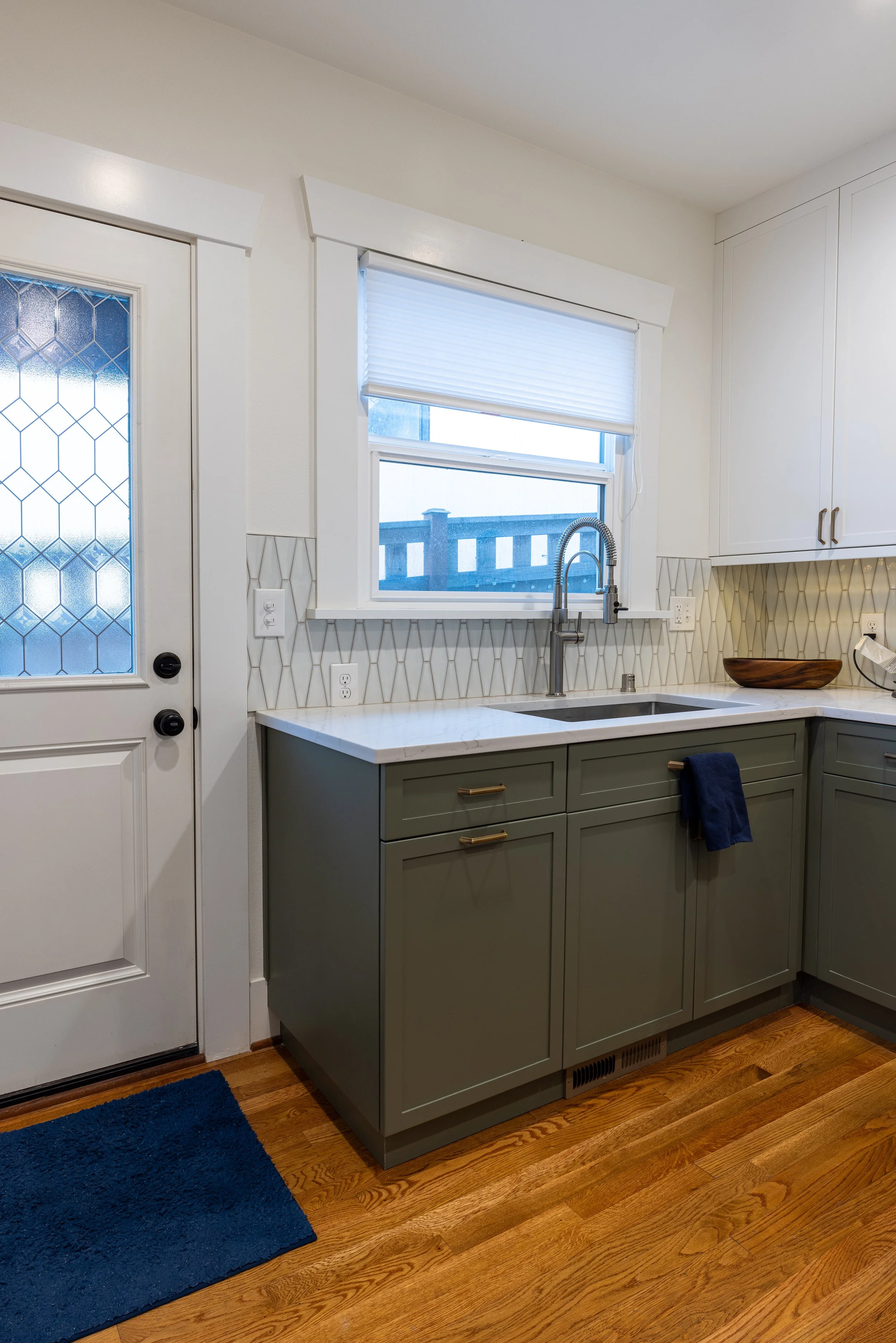 Green lower cabinets and white upper cabinets, quartz countertops, tile backsplash