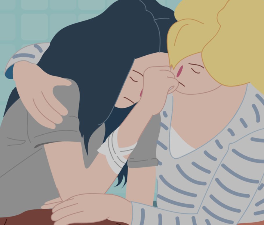 Two women comforting each other in a hospital or care setting, one with dark hair and the other with blonde hair, sharing an emotional moment.