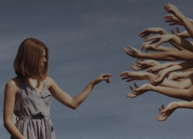 A girl with red hair reaches out to a crowd of outstretched hands against a blue sky.