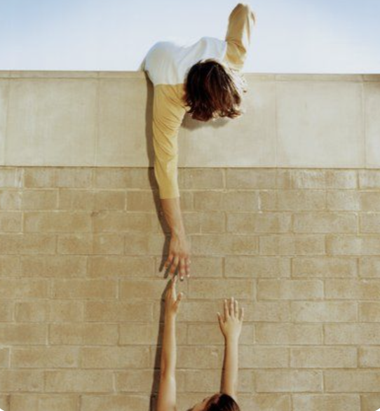 Person reaching down from a wall to help another person climb up.