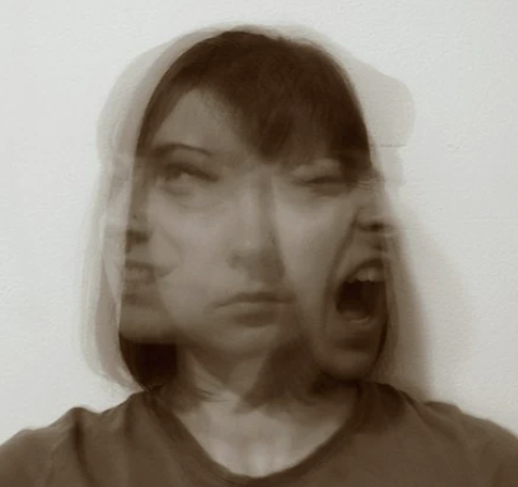 A woman making a facial expression that appears to be a combination of annoyance and anger, against a plain white wall.