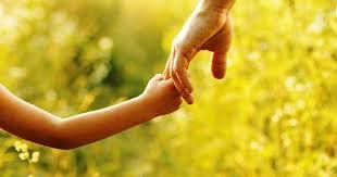 A child's hand holding an adult's hand outdoors with a blurred yellow and green background