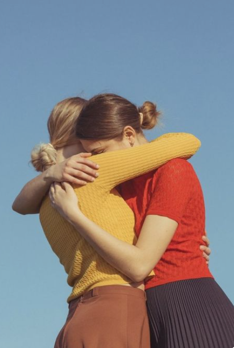 Two women with their hair in buns hugging each other against a clear blue sky.