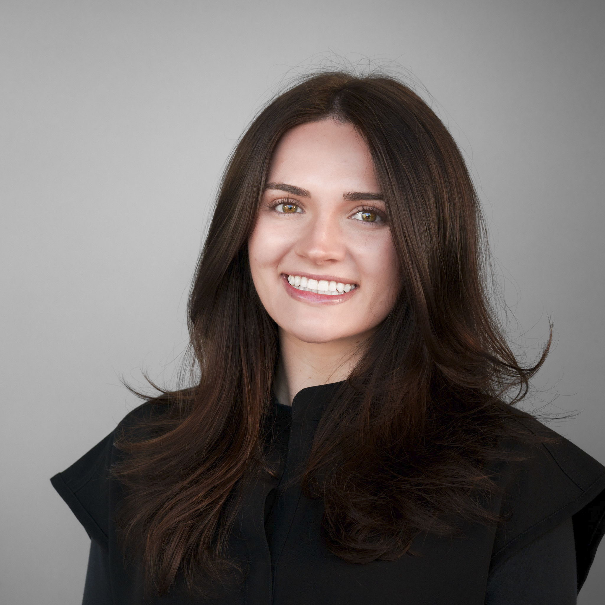 Smiling person with long brown hair standing in front of a stone wall.
