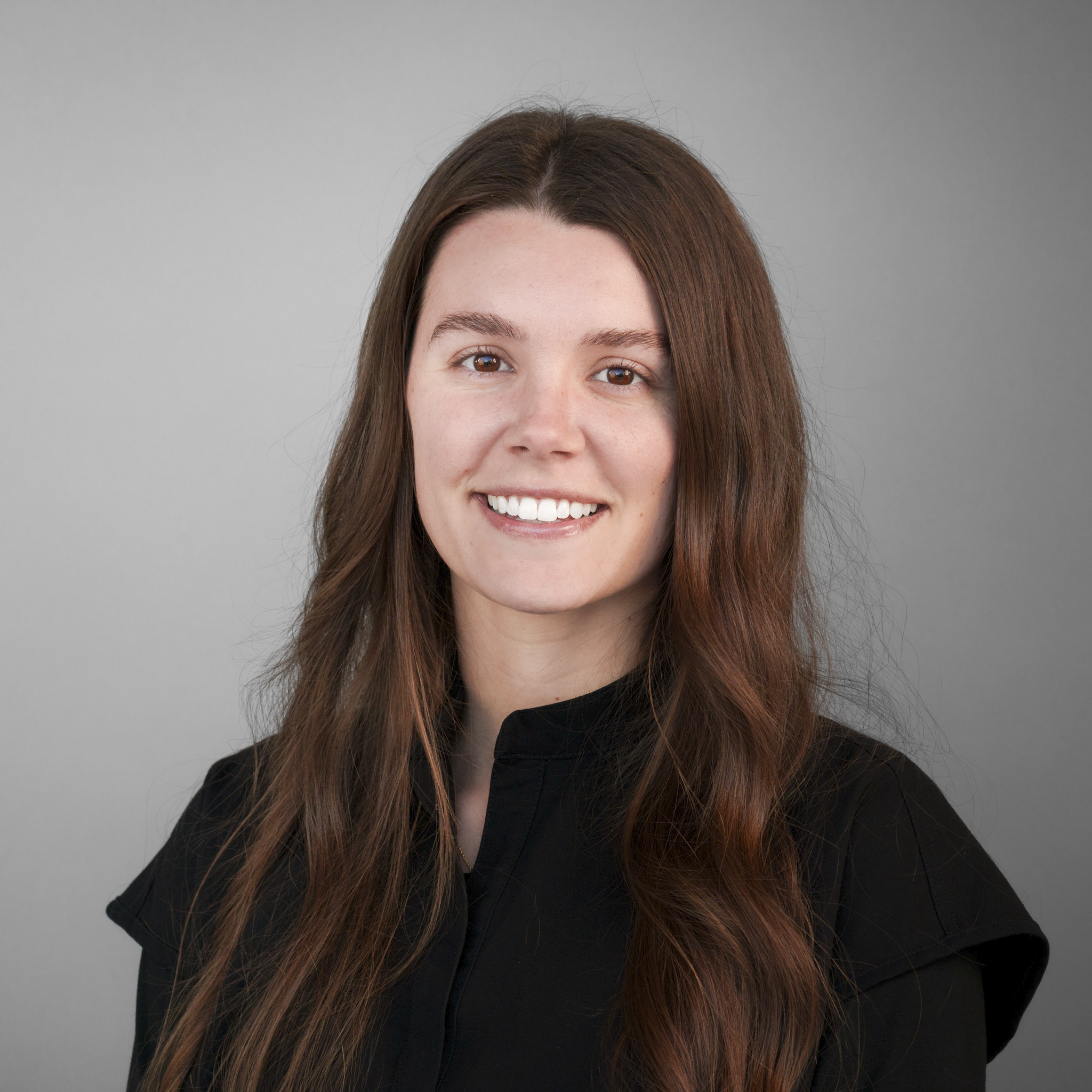 Smiling person with long brown hair in front of a stone wall.