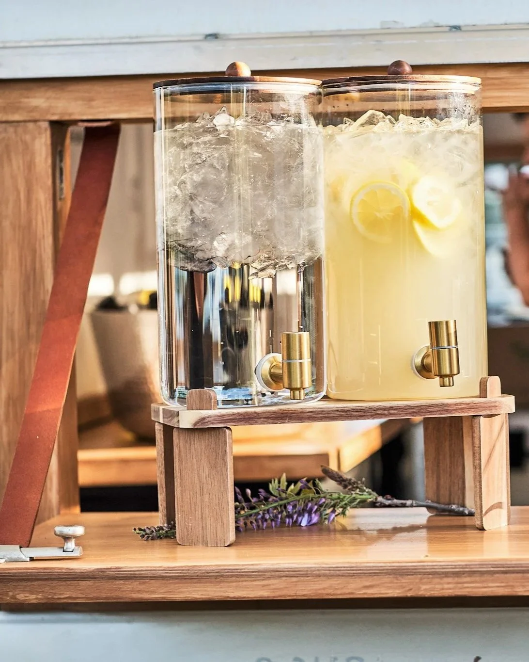 Two glass beverage dispensers on a wooden stand, one filled with water and ice, the other with lemon slices and lemonaid. Outdoor setting for events in Fallbroook, CA. Towing Temptations Mobile Bar Trailer