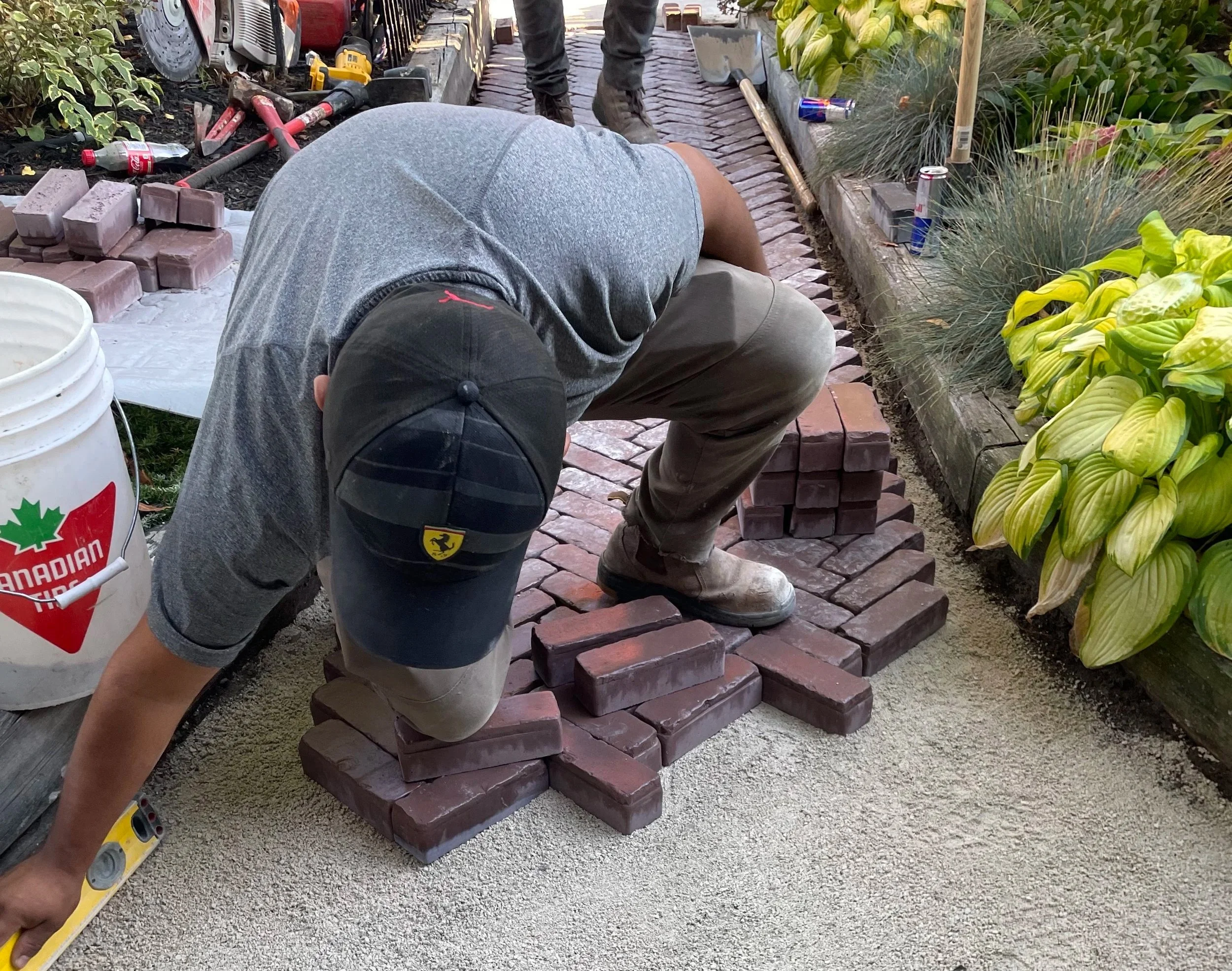 Worker installing Unilock Copthorne Burgundy Red pavers in a herringbone pattern with a Basalt border at a Beaches Toronto home.