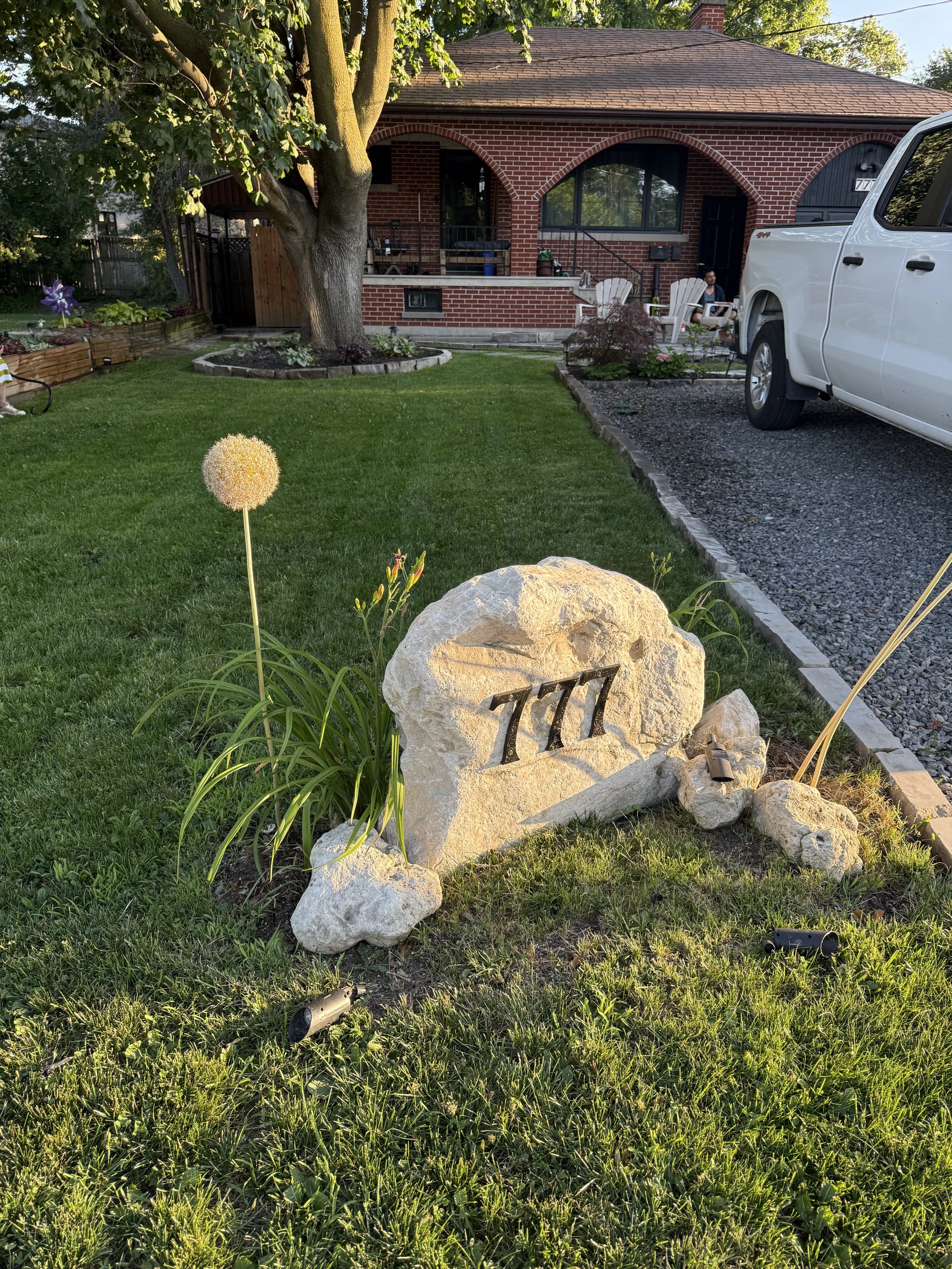 Garden rock with house numbers in an Etobicoke front yard, surrounded by blooming alliums and fresh landscape planting.
