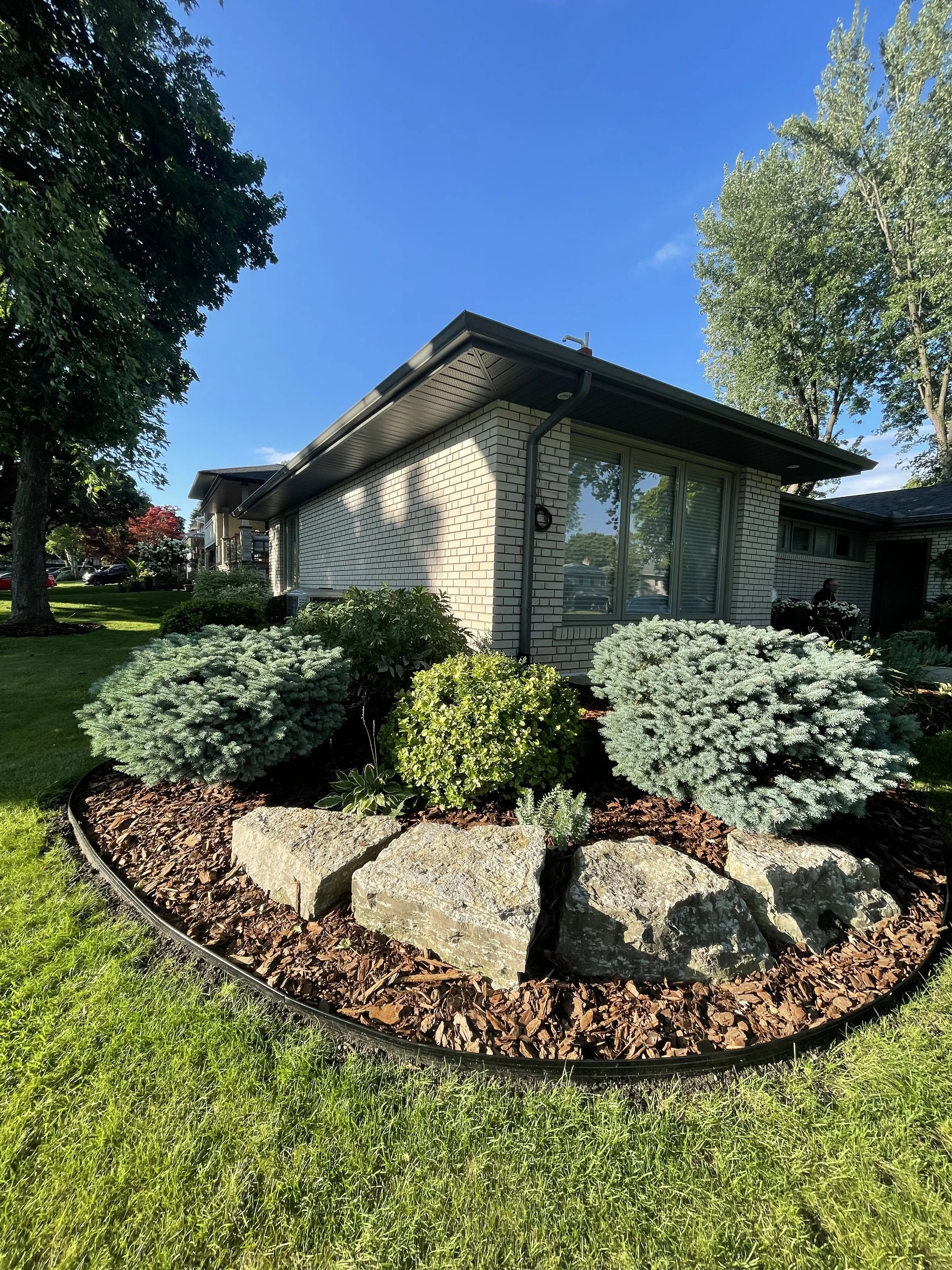 Freshly mulched garden beds with pine nuggets and black aluminum edging in an Etobicoke front yard.