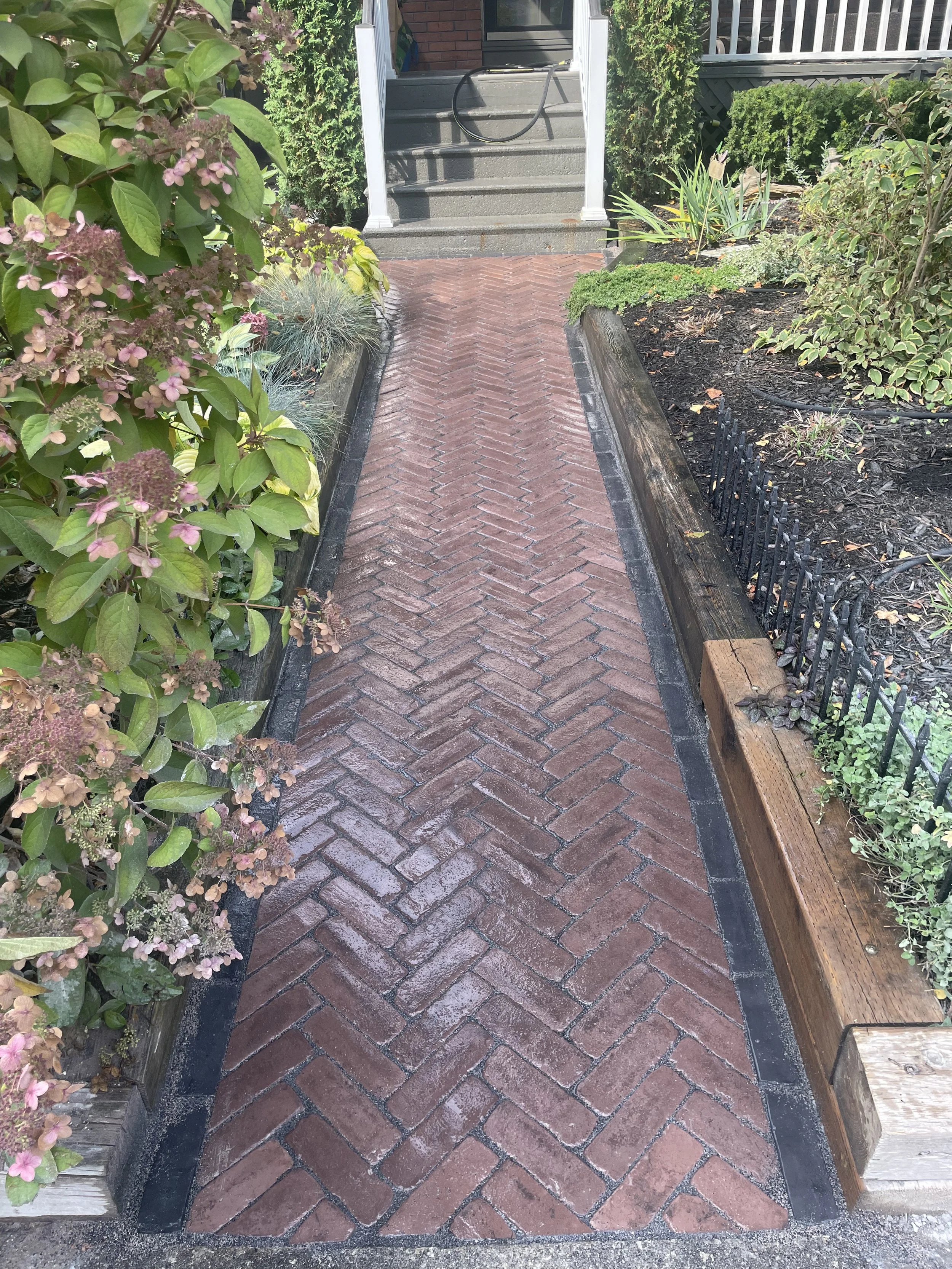 New Unilock Copthorne Burgundy Red herringbone walkway with a Basalt border installed at a red‑brick home in The Beaches, Toronto.