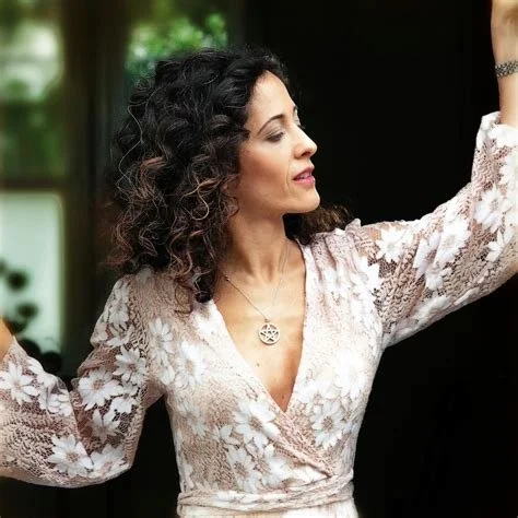 Woman with curly hair in a lace floral dress, raising her arm