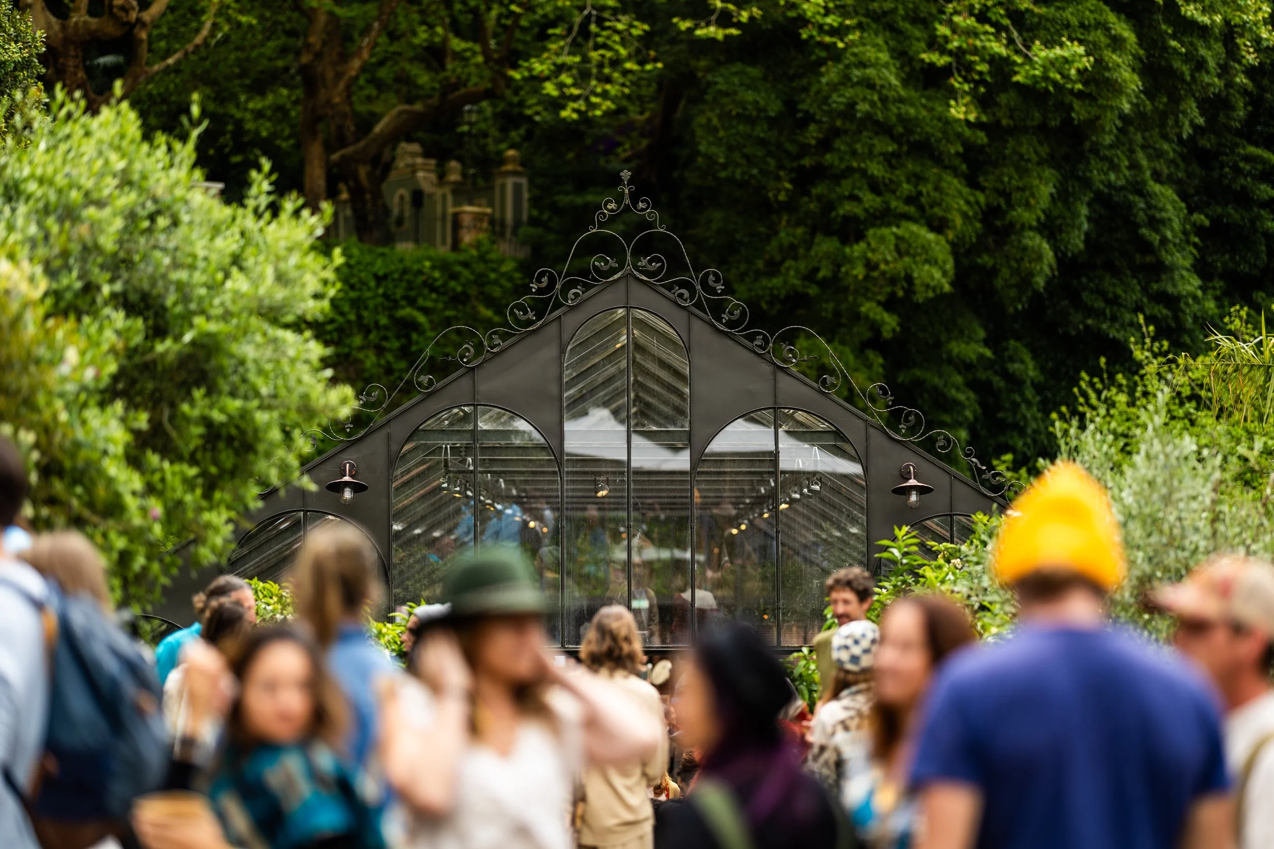 People gather outdoors near a glass greenhouse surrounded by lush green trees at the FiVth Summit In Portugal.