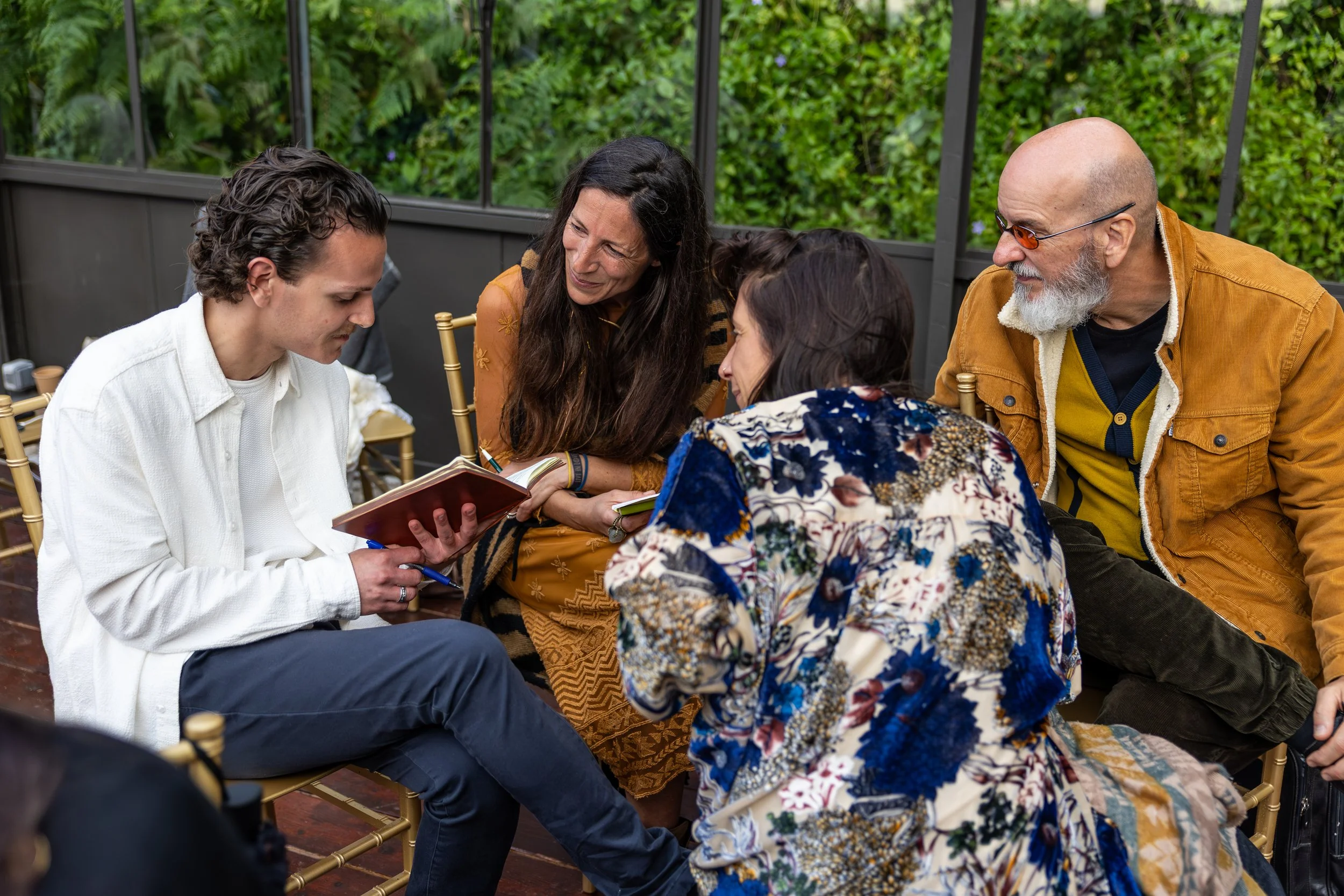 Group of four people sitting together on a patio, engaged in a conversation, with all four looking at a notebook or journal at the FiVth Experience in Portugal.
