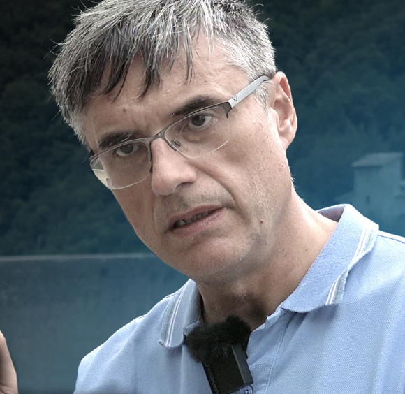 Filippo Biondi, man with glasses, short gray hair, wearing a light blue collared shirt outdoors with trees and a body of water in the background.