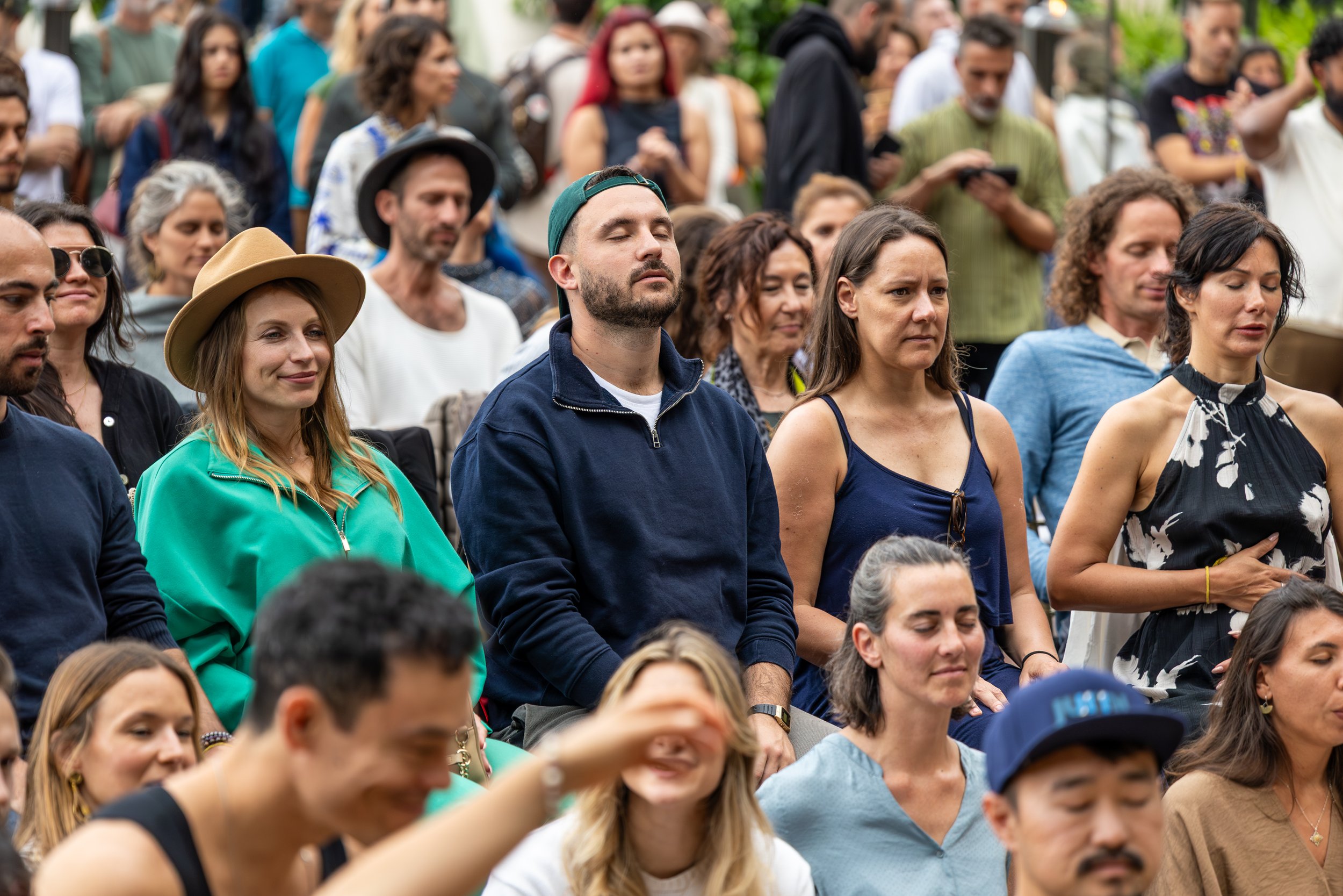 People seated outdoors, participating in a meditative or prayerful activity, with some eyes closed and hands resting on laps during a spiritual conference in Portugal.