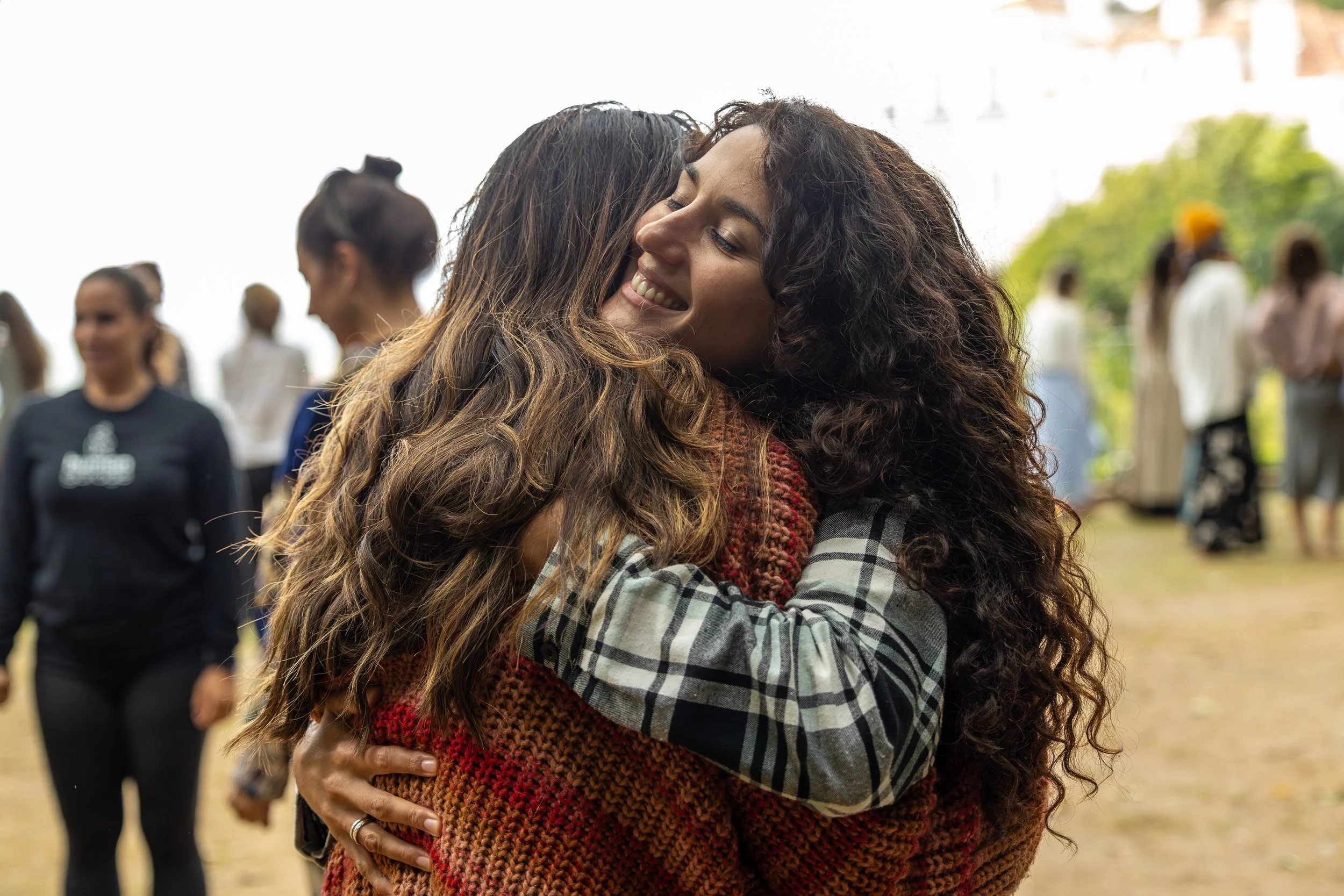 Two women hugging and smiling at an outdoor gathering with other people in the background at the FiVth Summit in Sintra, Portugal.
