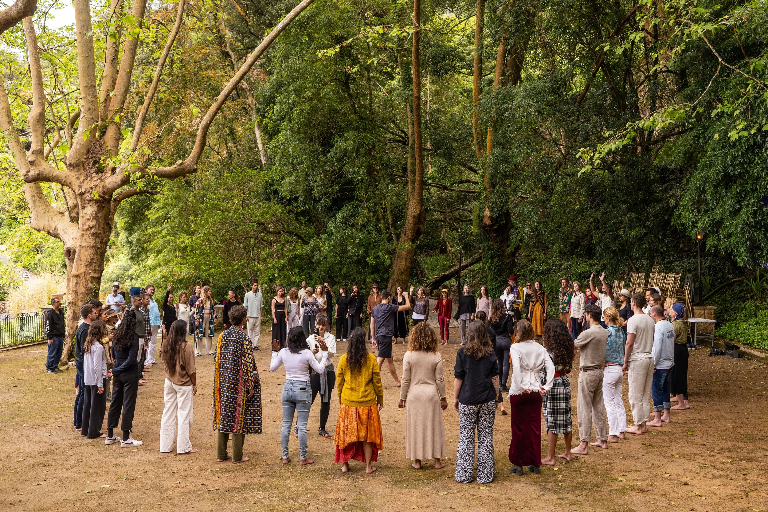 A large group of people gathered outdoors in a circle under tall trees, participating in a conscious event at the FiVth Summit in Portugal.
