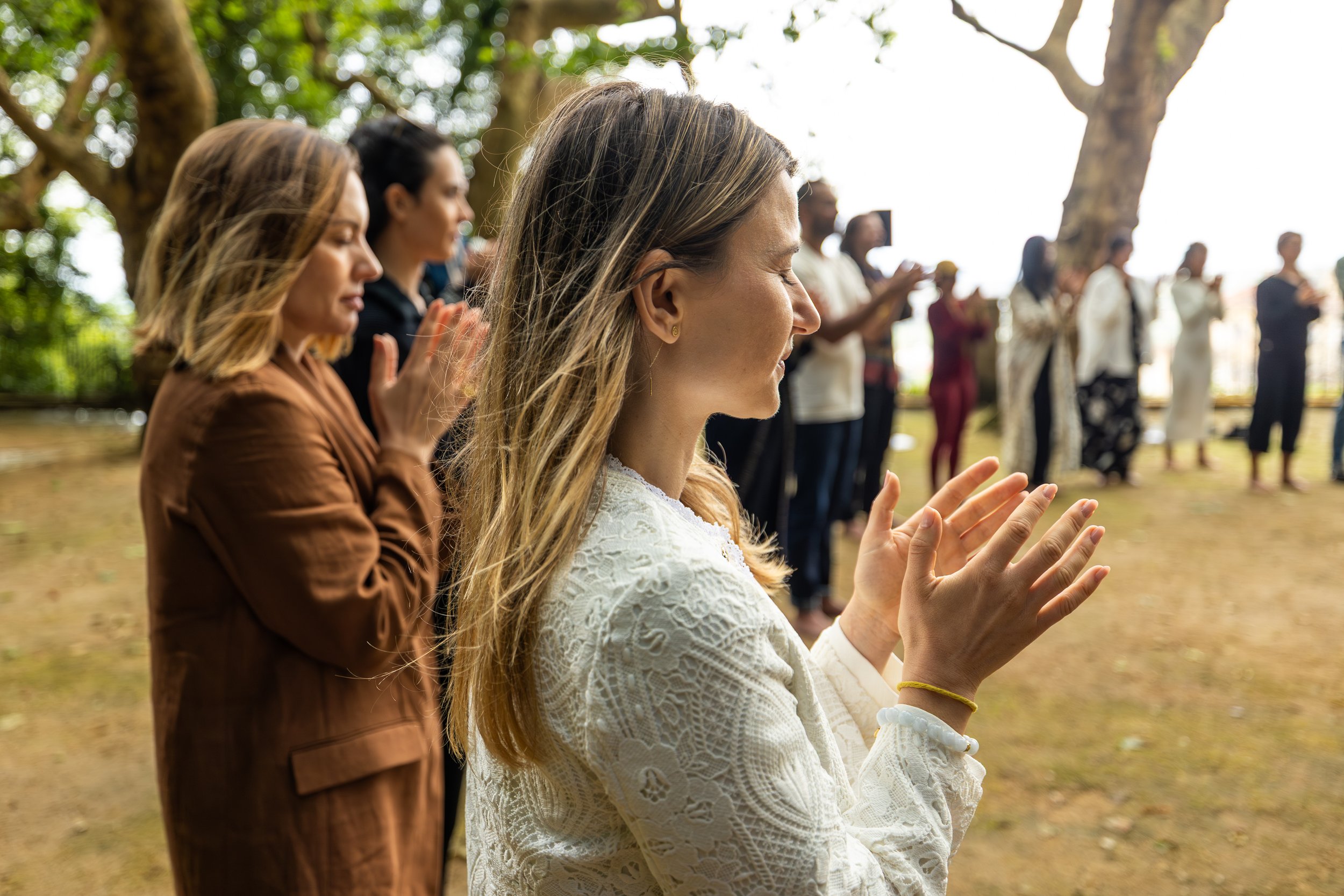 A group of people, mostly women, standing outdoors in prayer or meditation, with trees in the background at the FiVth Summit 2025 in Portugal.