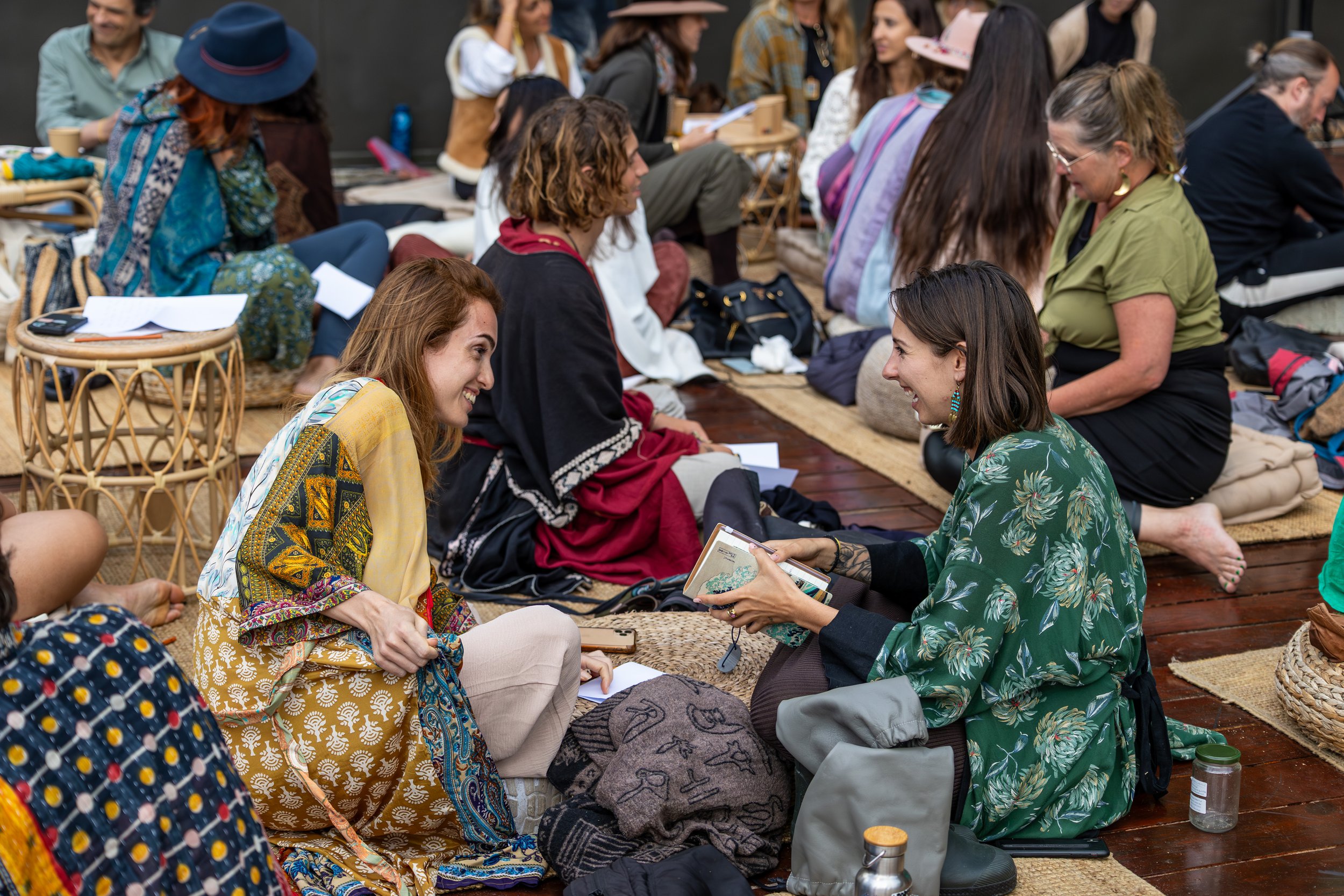 Conscious Community Gathering—People sitting on rugs and cushions, engaged in conversations, in a cozy indoor setting.