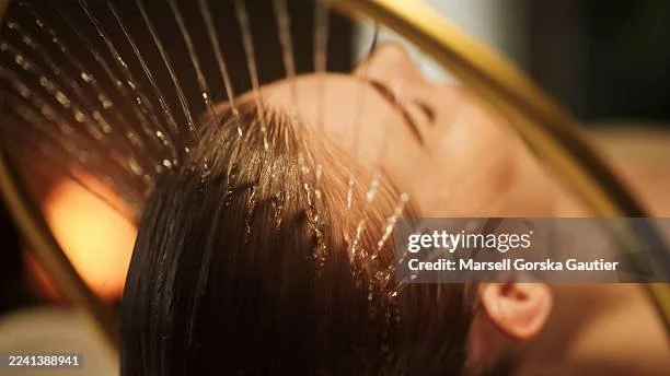 En person har vannstråler rettet mot hodet over en dusjhode.