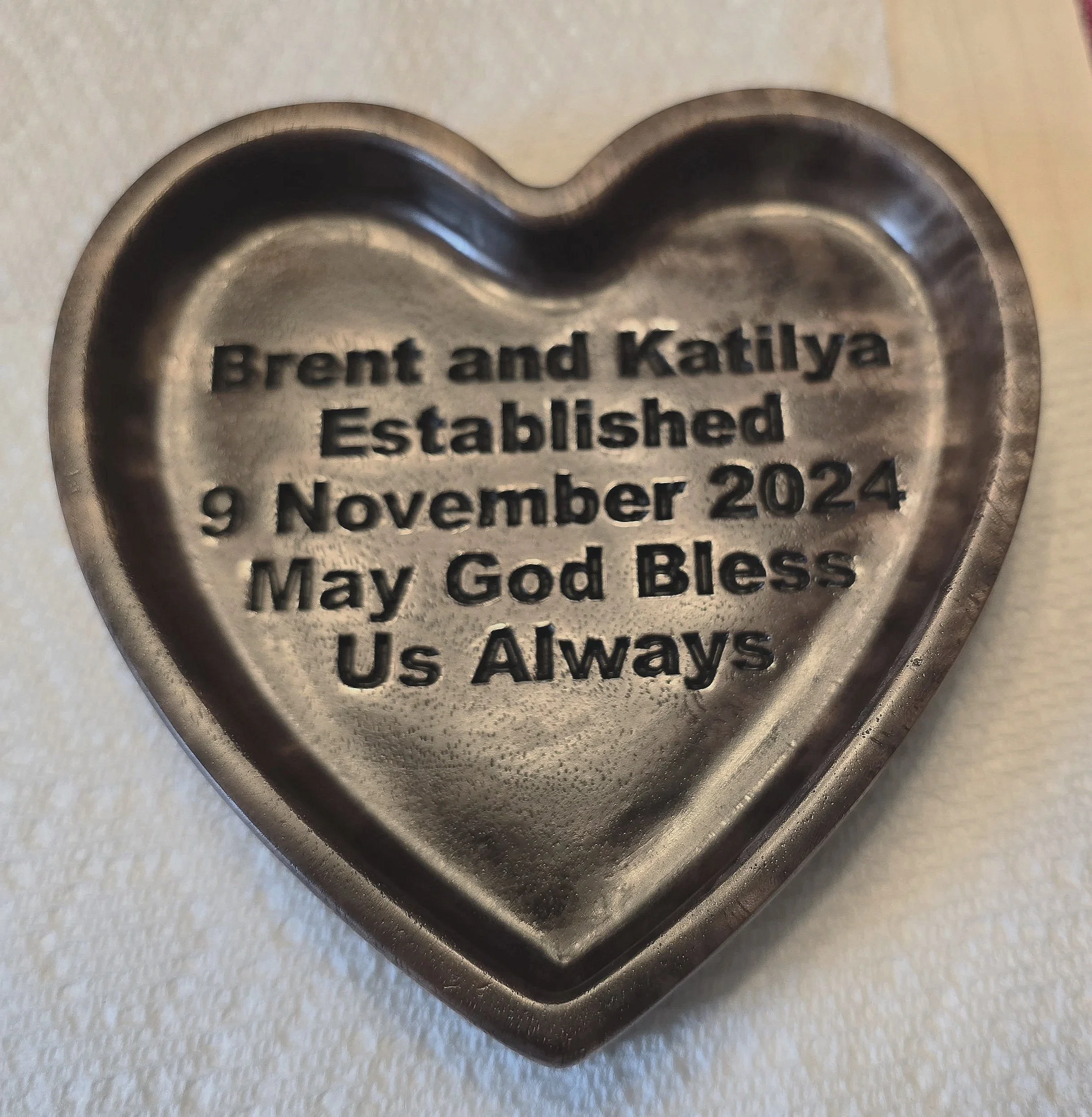 Heart-shaped metal keepsake with engraved text about Brent and Katiya's wedding date and blessing