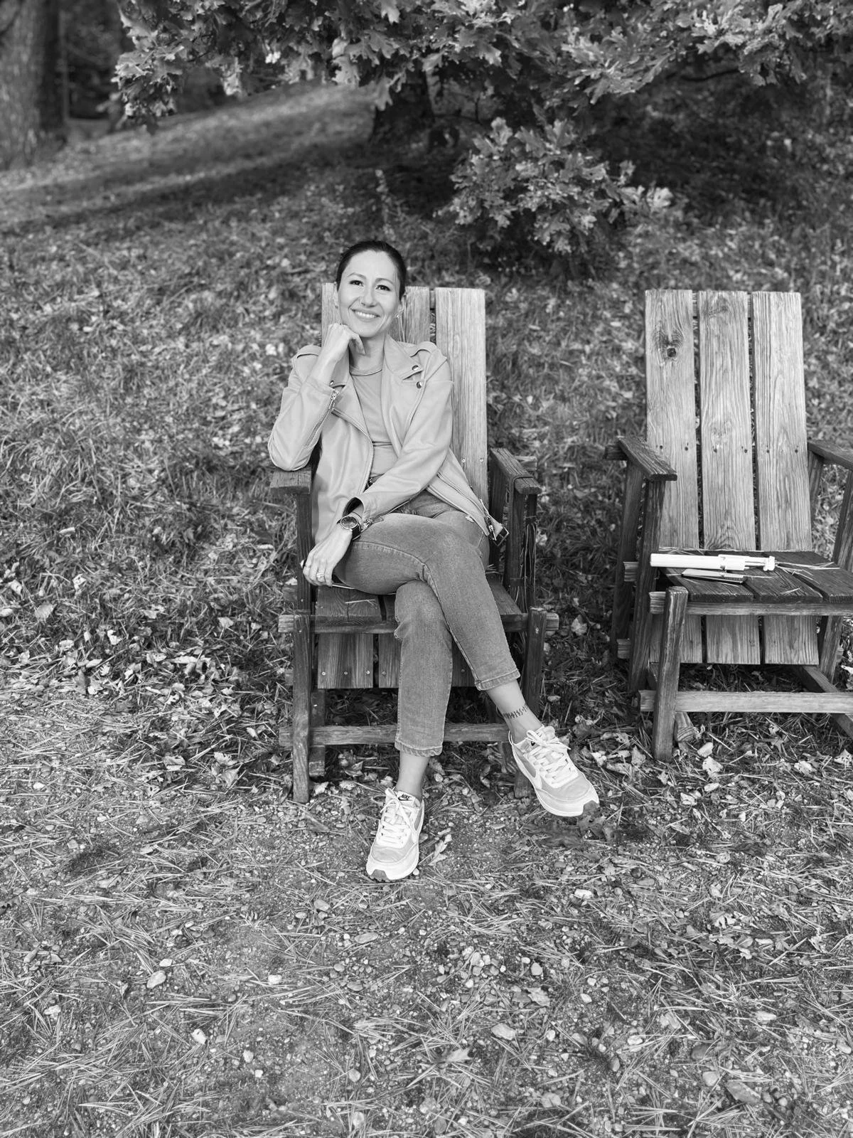 Mujer sonriente sentada en silla de madera en entorno natural, fotografía en blanco y negro que representa bienestar mental, mindfulness y conversación interna positiva para blog de amor propio.