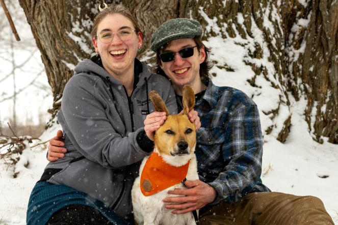 A happy couple with a dog outdoors in a snowy forest.