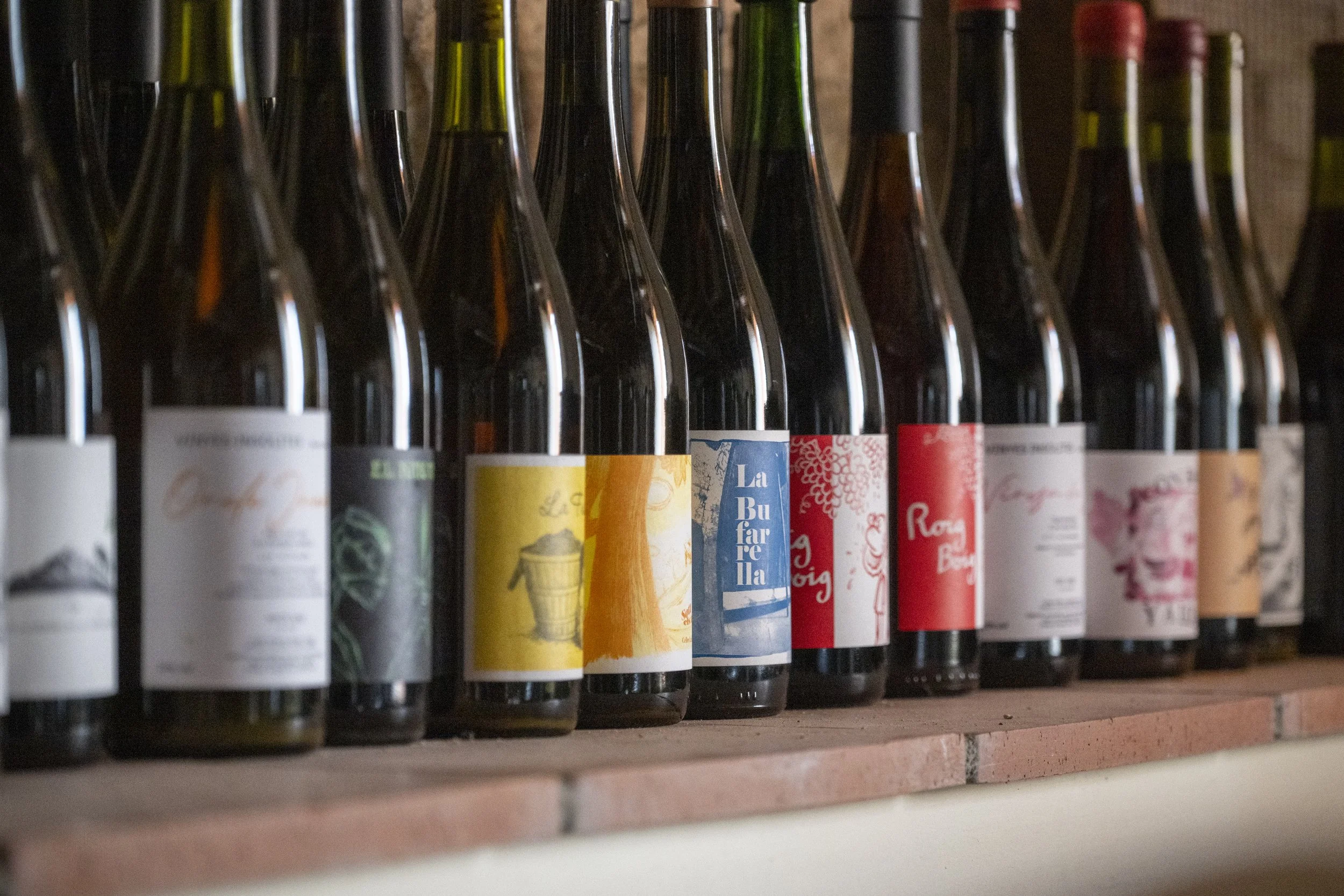 Rows of wine bottles on a wooden shelf with colorful labels.