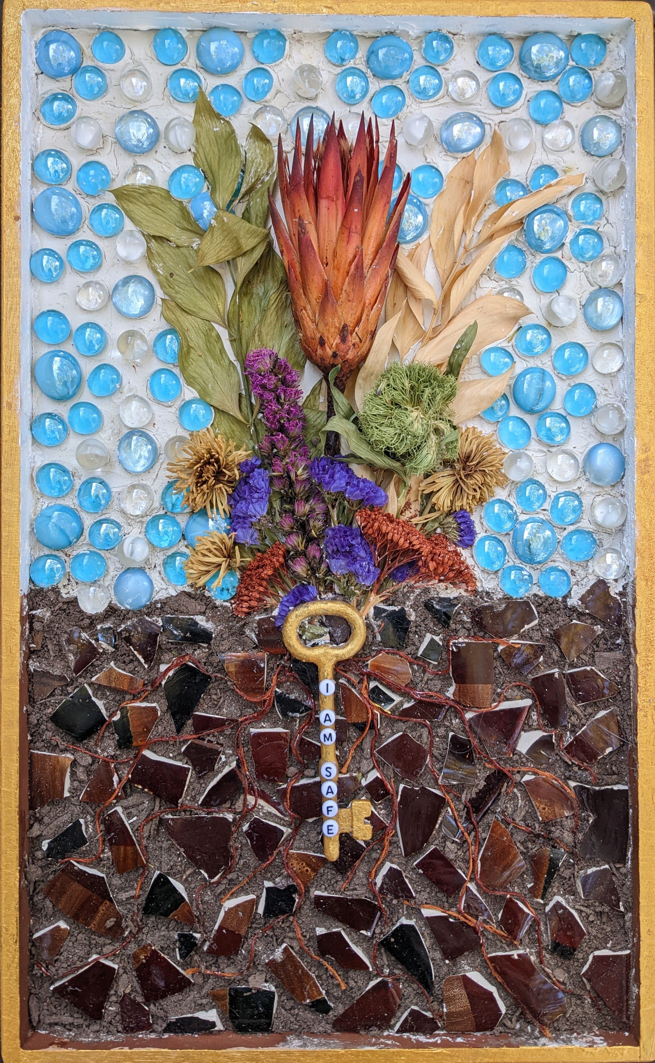Mixed-media artwork featuring dried flowers, colorful glass stones, and mosaic pieces with a gold key engraved with the words 'I AM SAFE'