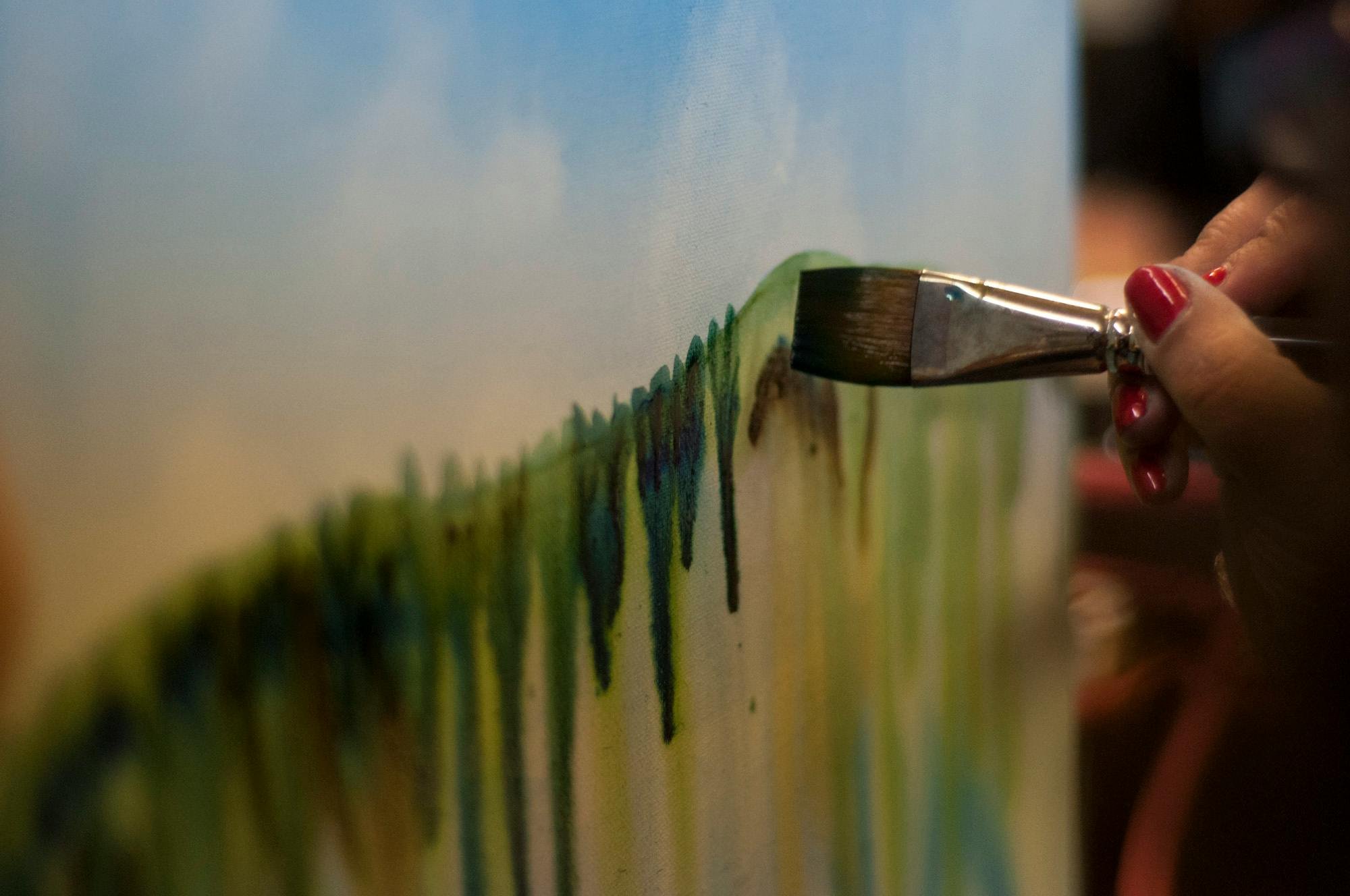 Close-up of a person painting on a canvas with a broad brush, creating colorful drips and streaks.