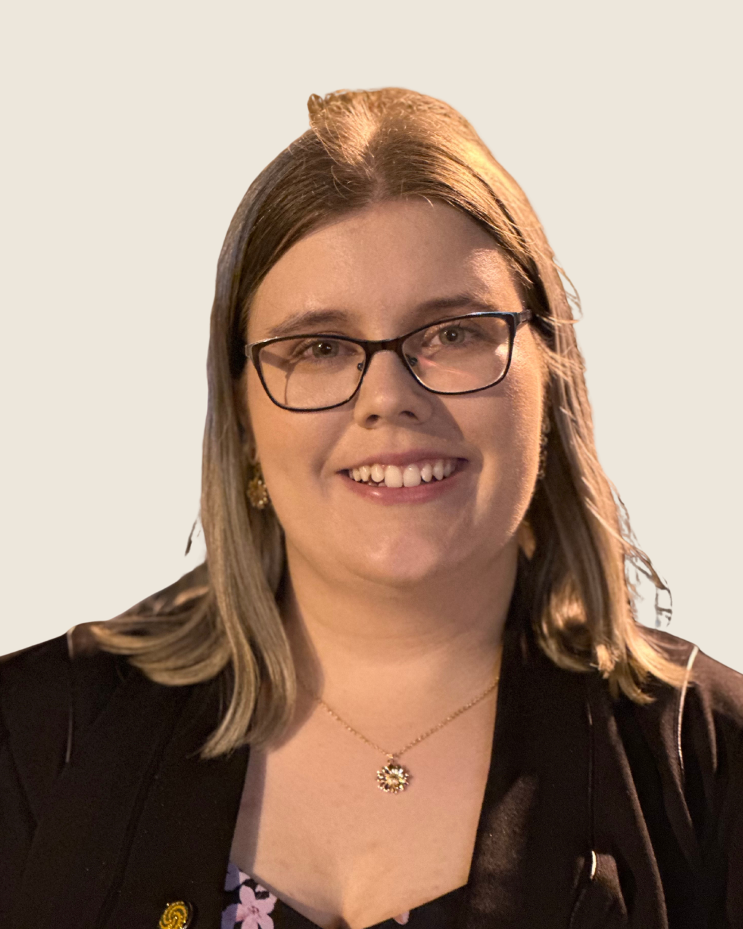 A woman with brown hair, blue eyes, and a septum piercing, smiling, wearing a black-colored shirt, against a plain background.