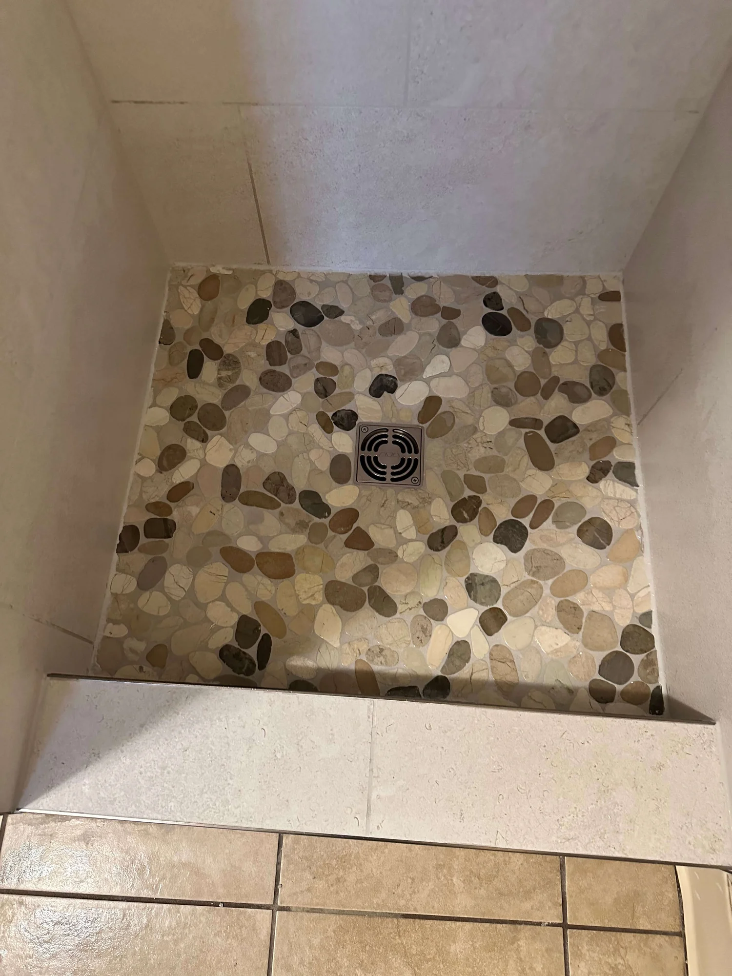 Pebble stone shower pan sloped to a center drain in a Logan tile shower