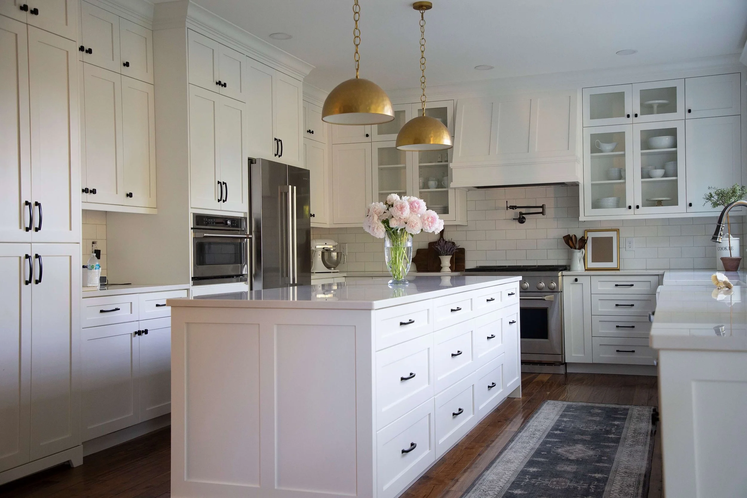 White kitchen remodel with a large island, brass pendant lights, and glass-front cabinets by ONYX Bros in Cache Valley, Utah
