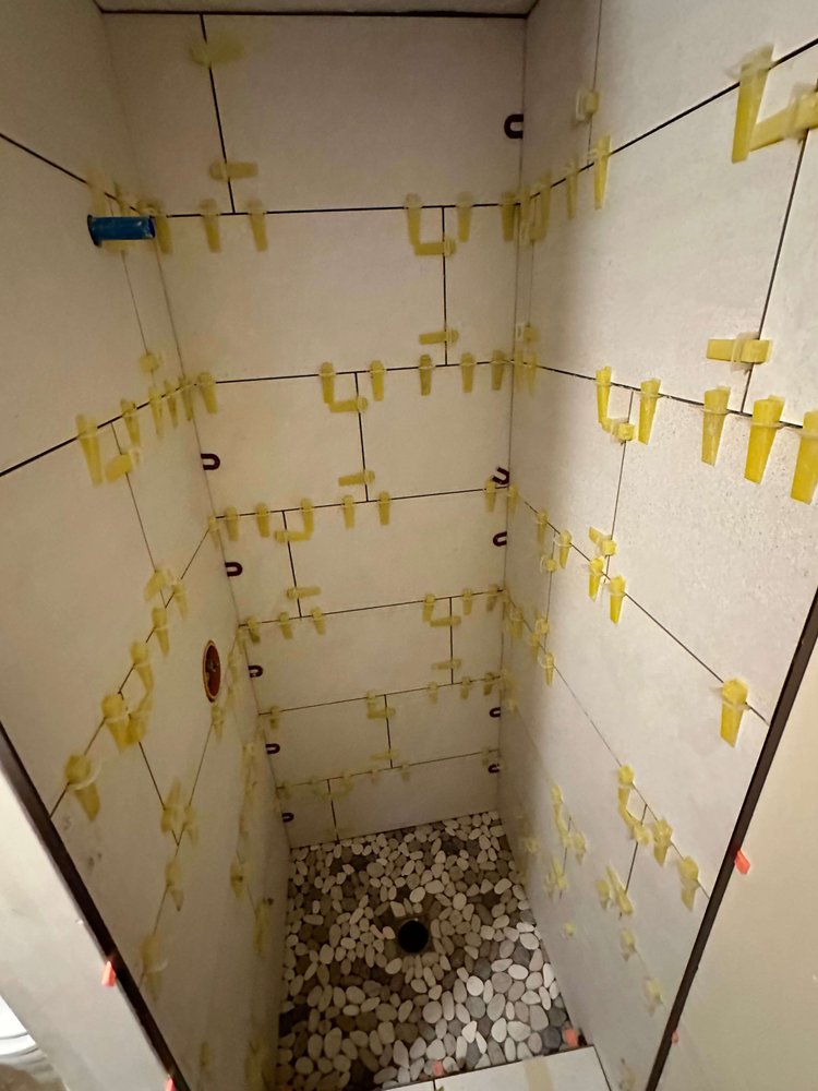 Large-format wall tile being set with spacers over a pebble shower floor
