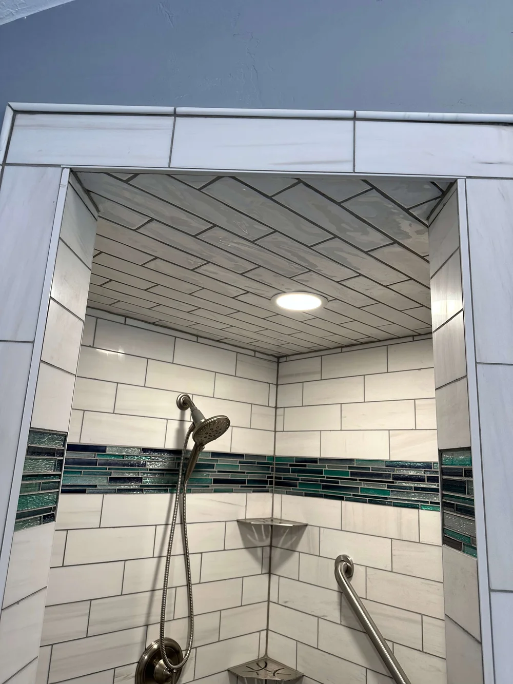 Tiled shower with a herringbone tile ceiling, white subway walls, and a teal glass accent band in Logan