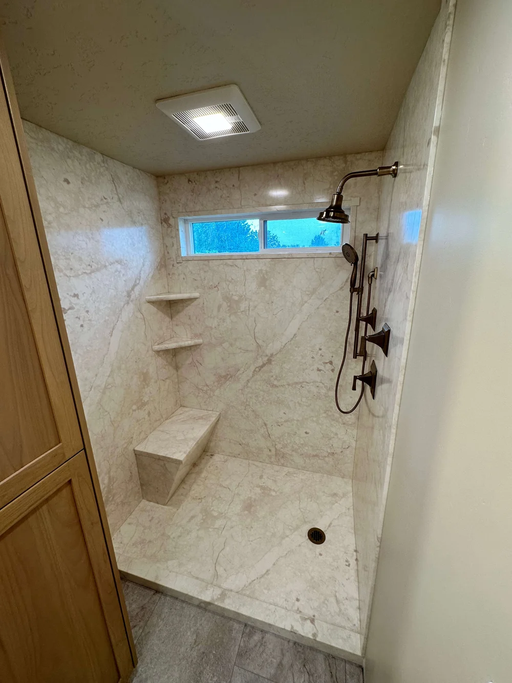 Marble-look tile shower with a built-in bench, corner shelves, and a window in a Cache Valley home