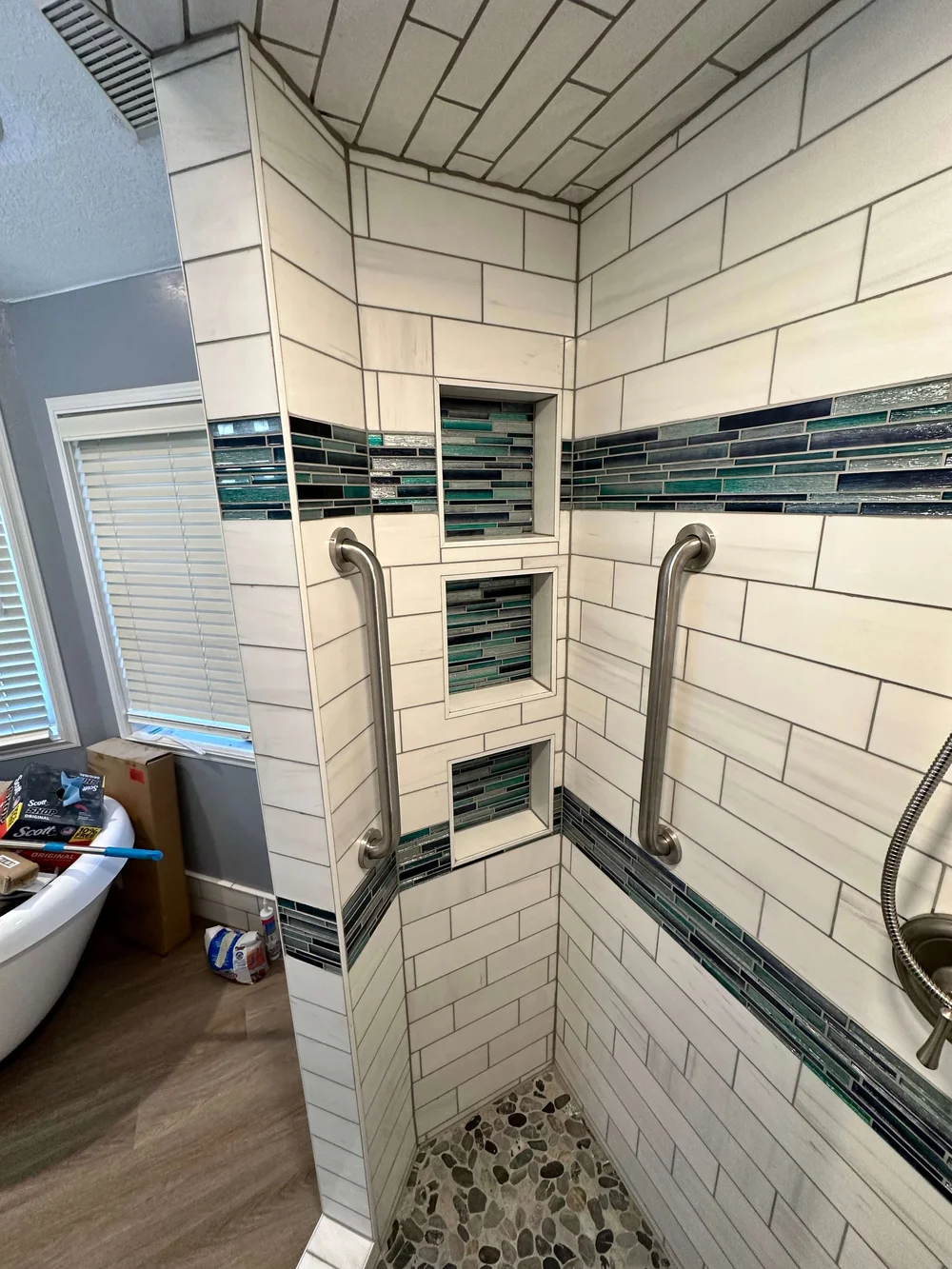 White subway tile shower with blue mosaic niches, grab bars, and a pebble floor in Logan, Utah