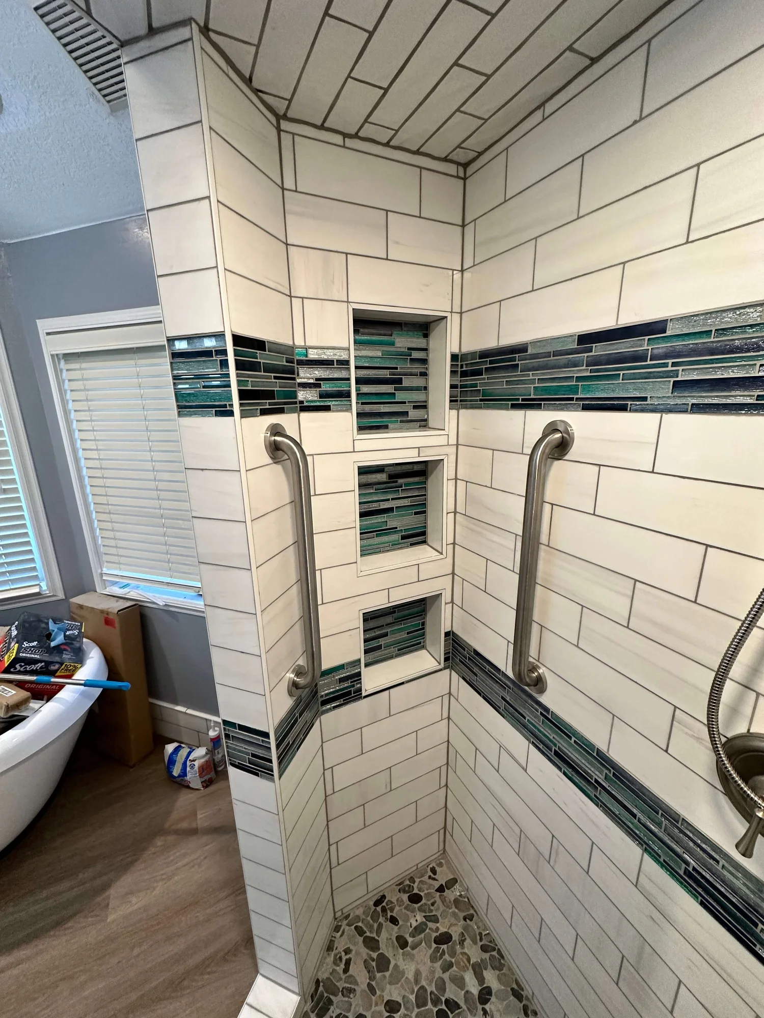 Finished subway tile shower with blue mosaic niches and a pebble floor by a Logan tile installer