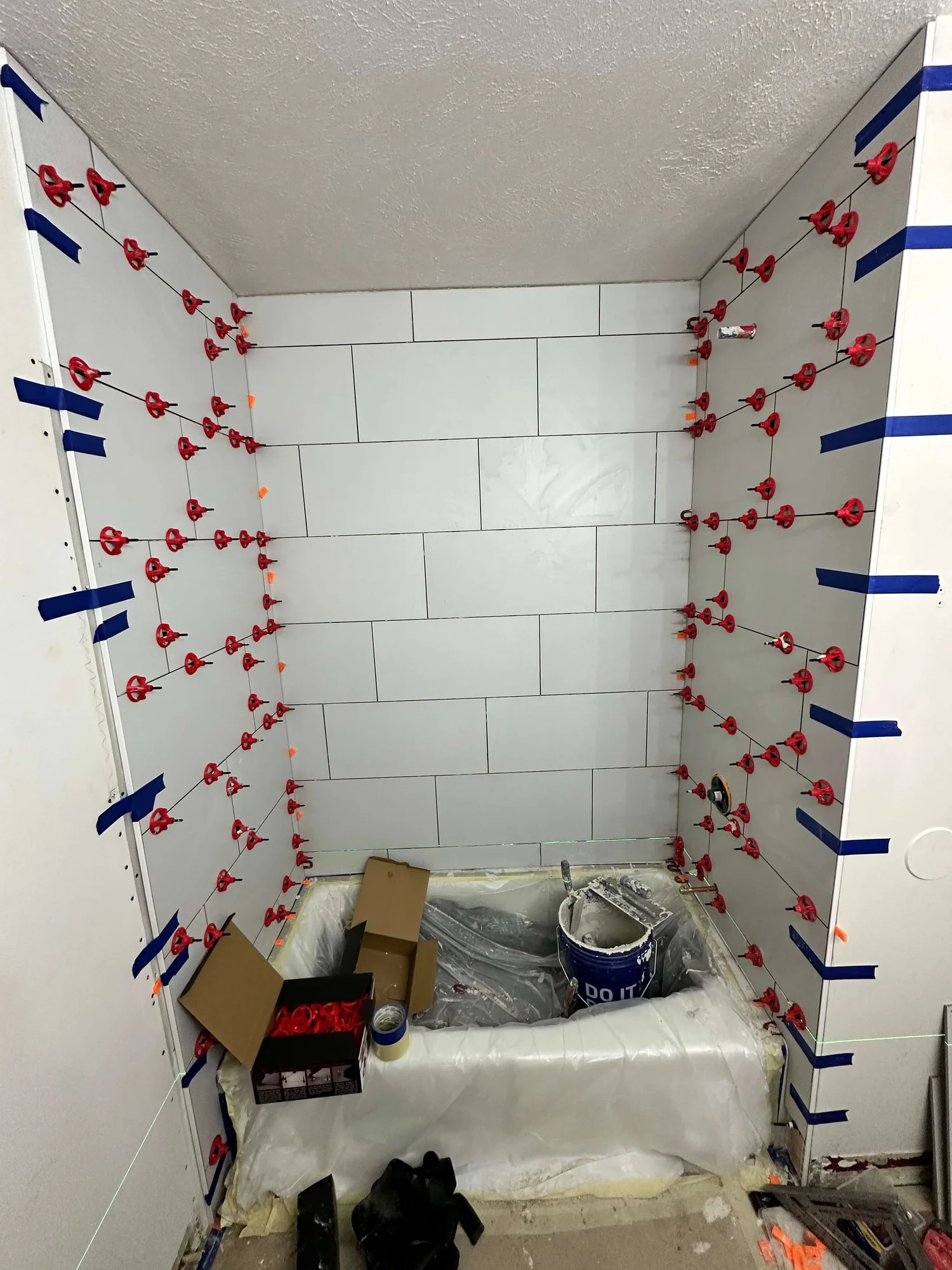 Tub surround tile going up with leveling clips in a Logan bathroom
