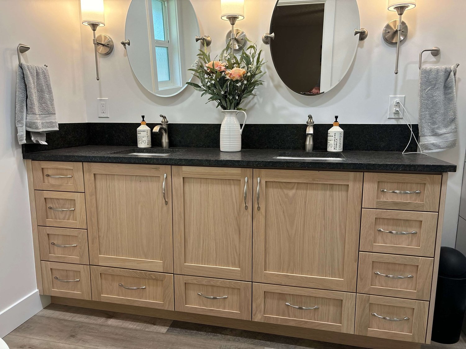 Double vanity with light wood cabinets, black countertop, and round mirrors in a Logan bathroom remodel
