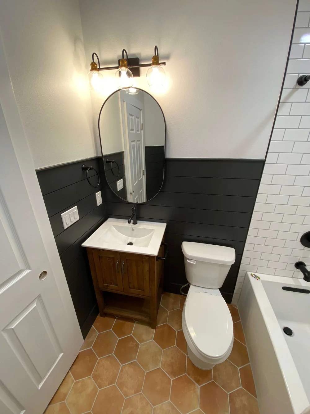 Logan bathroom remodel with an arched mirror, wood vanity, dark wainscot, and hexagon terracotta floor tile